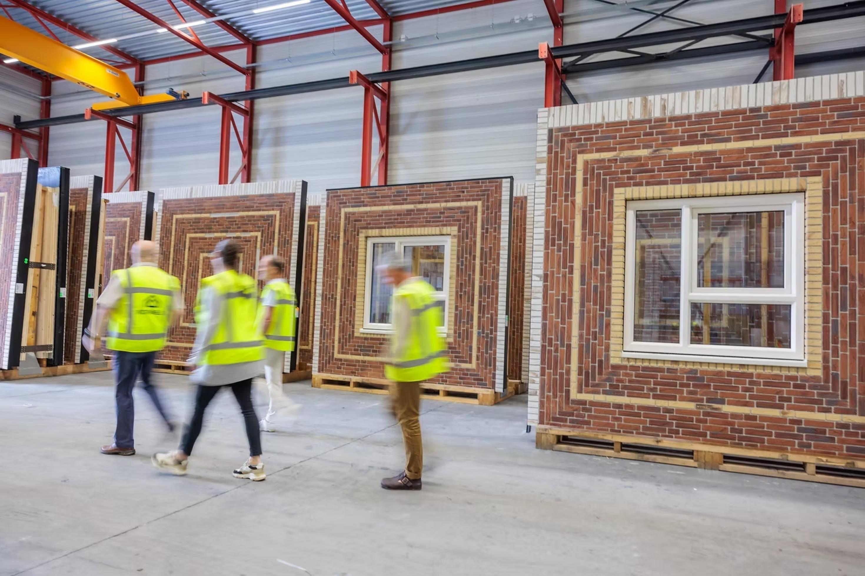 Drei Elemente einer Klinkerfassade mit integriertem Fenster in einer Fabrik, davor vier Menschen