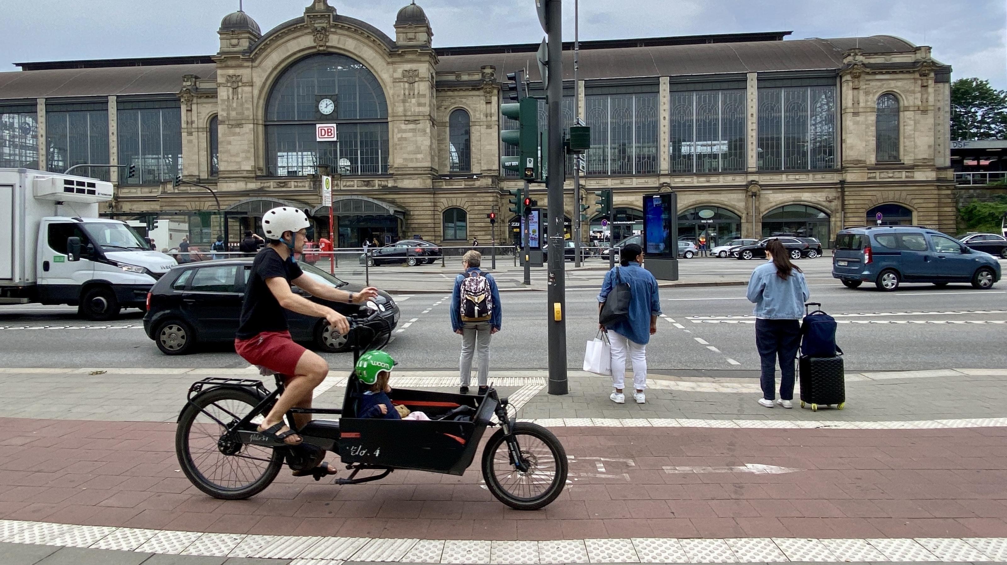 Ein Mann fährt ein Kind im Lastenrad durch die Stadt