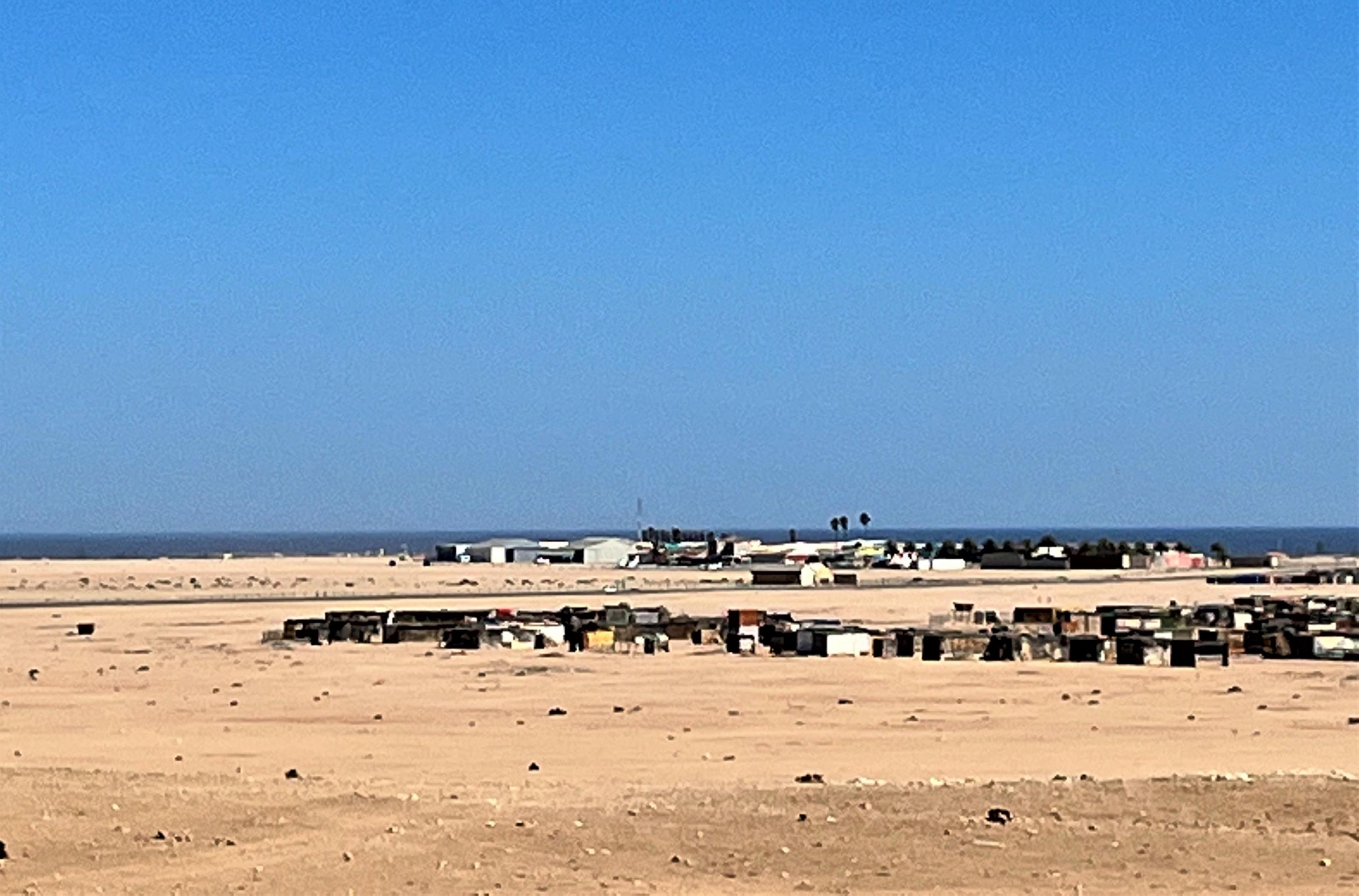 Kleine Häuschen stehen in einer trostlosen Wüstenlandschaft an der Küste