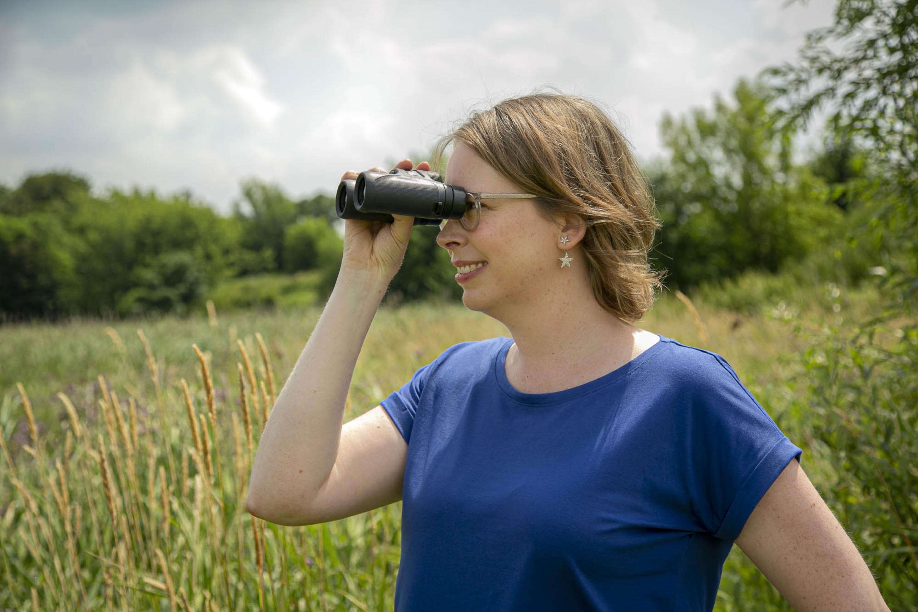 Silke Hartmann blickt durchs Fernglas über eine offene Landschaft