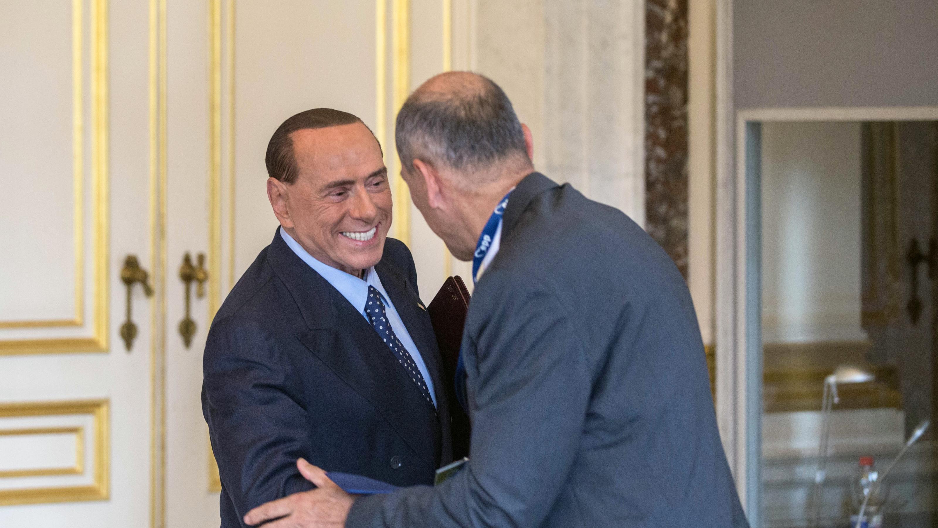 Silvio Berlusconi schüttelt grinsend einem Mann die Hand