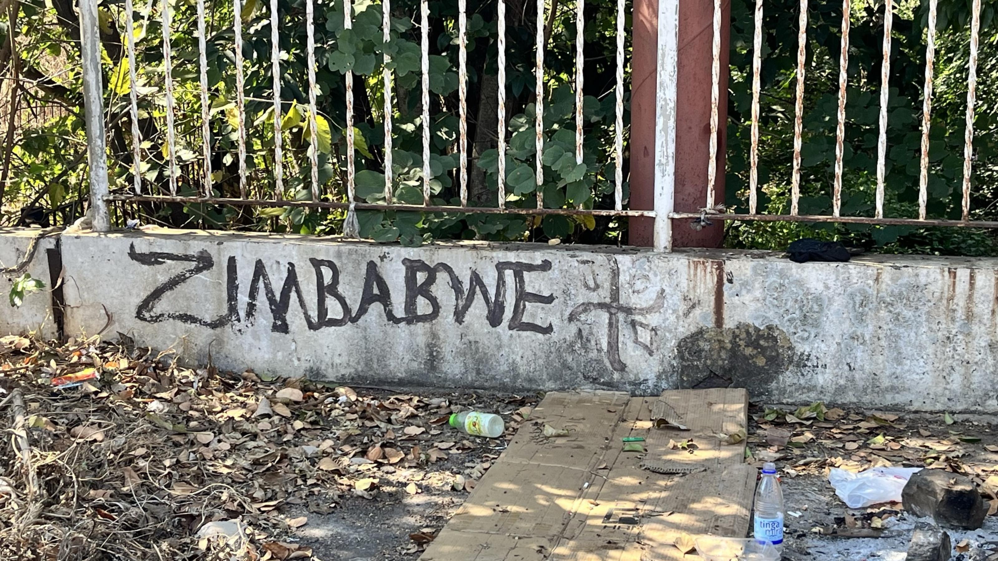 Auf eine Mauer hat jemand Zimbabwe geschrieben. Davor liegt Müll.