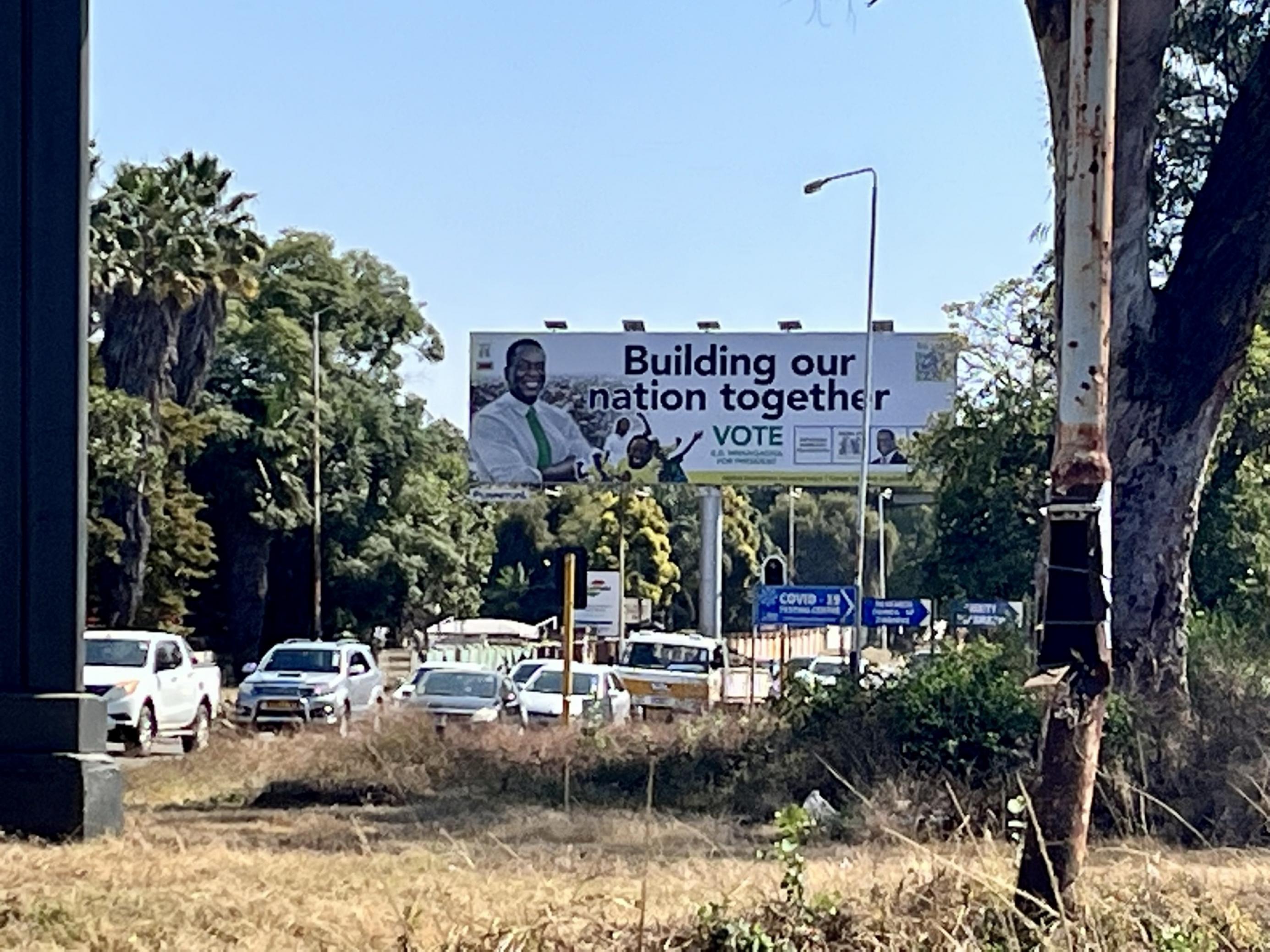 Über der Straße hängt das Wahlplakat der Regierungspartei, darunter staut sich der Verkehr, die Straßenbeleuchtung ist verrostet.