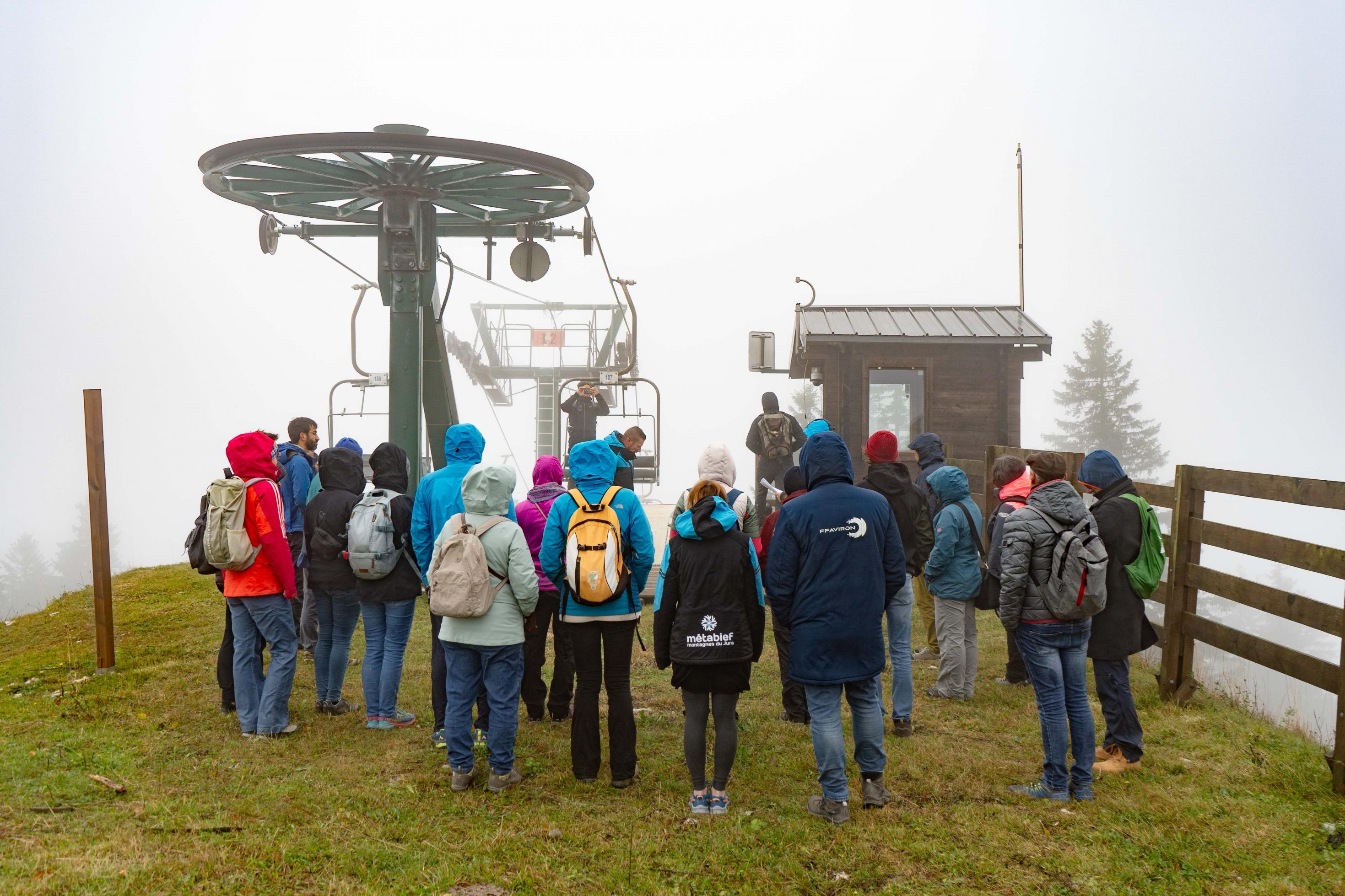 eine gruppe Menschen von hinten vor einem Schlepplift, dahinter Nebel