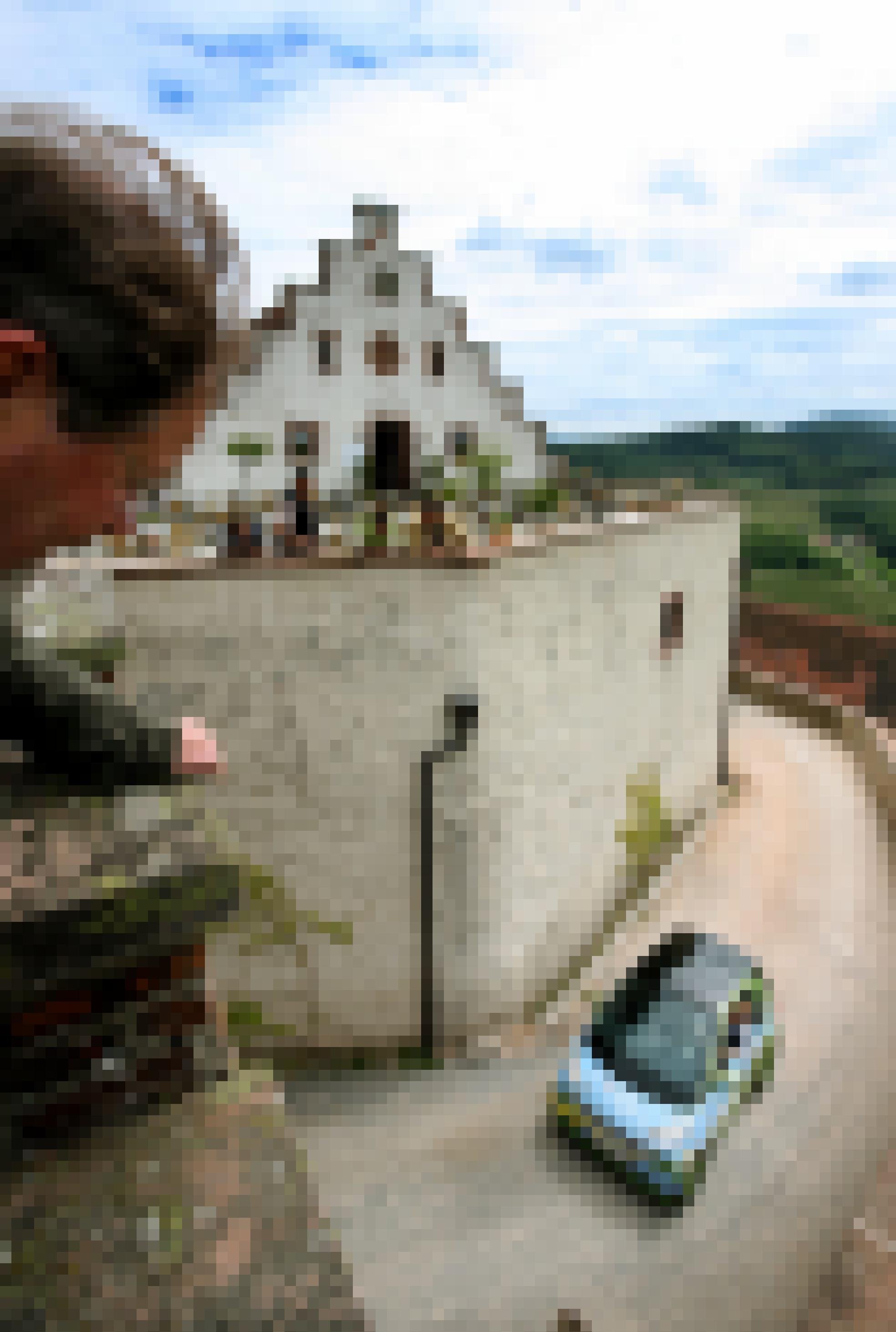 Ein elektrischer Smart fährt einen Berg hinauf. Oben schaut ein Mann über eine Schlossmauer auf den Weg.