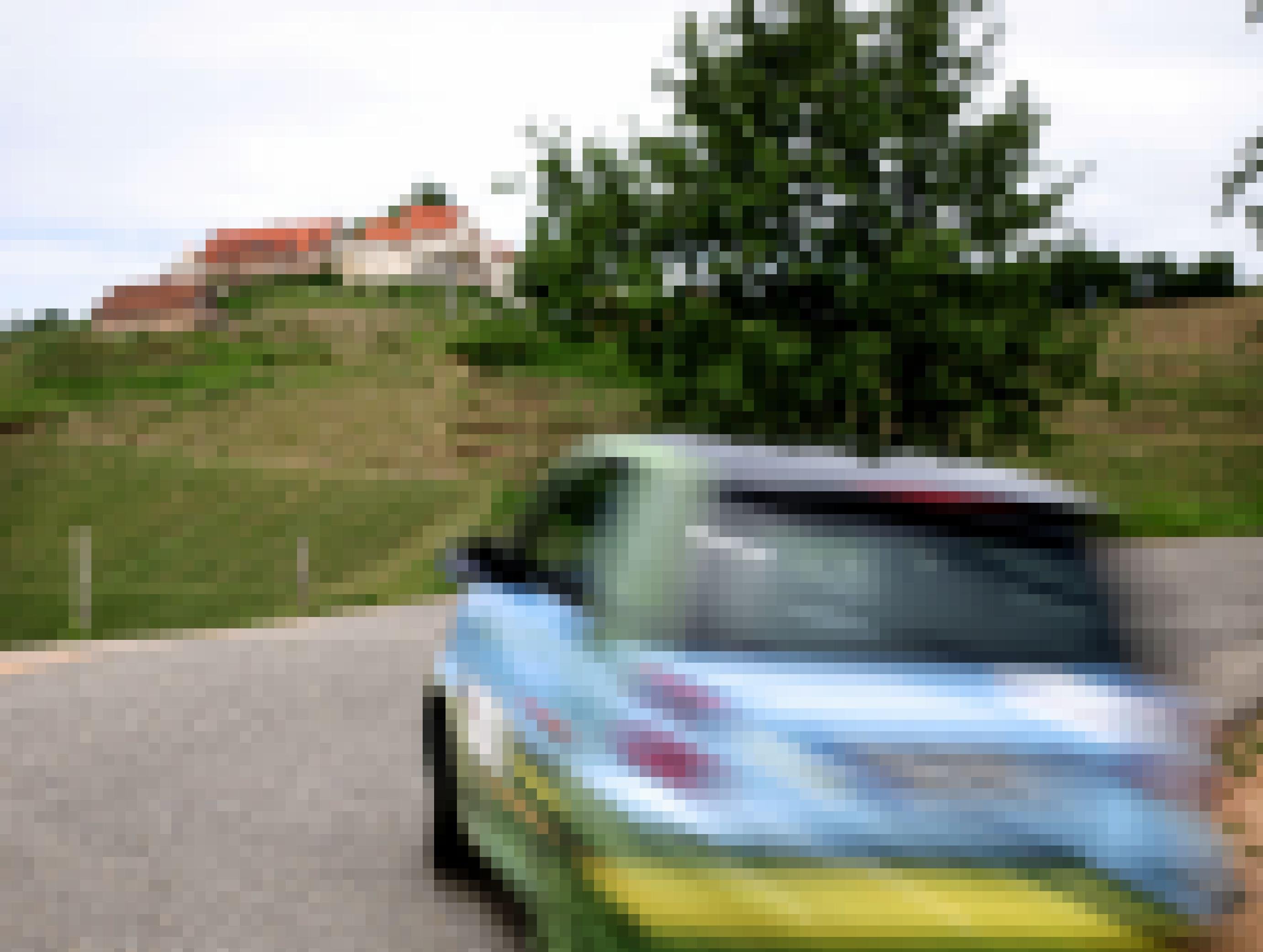 Ein kleines Elektroauto fährt über eine Landstraße. Weinberge sind zu sehen.