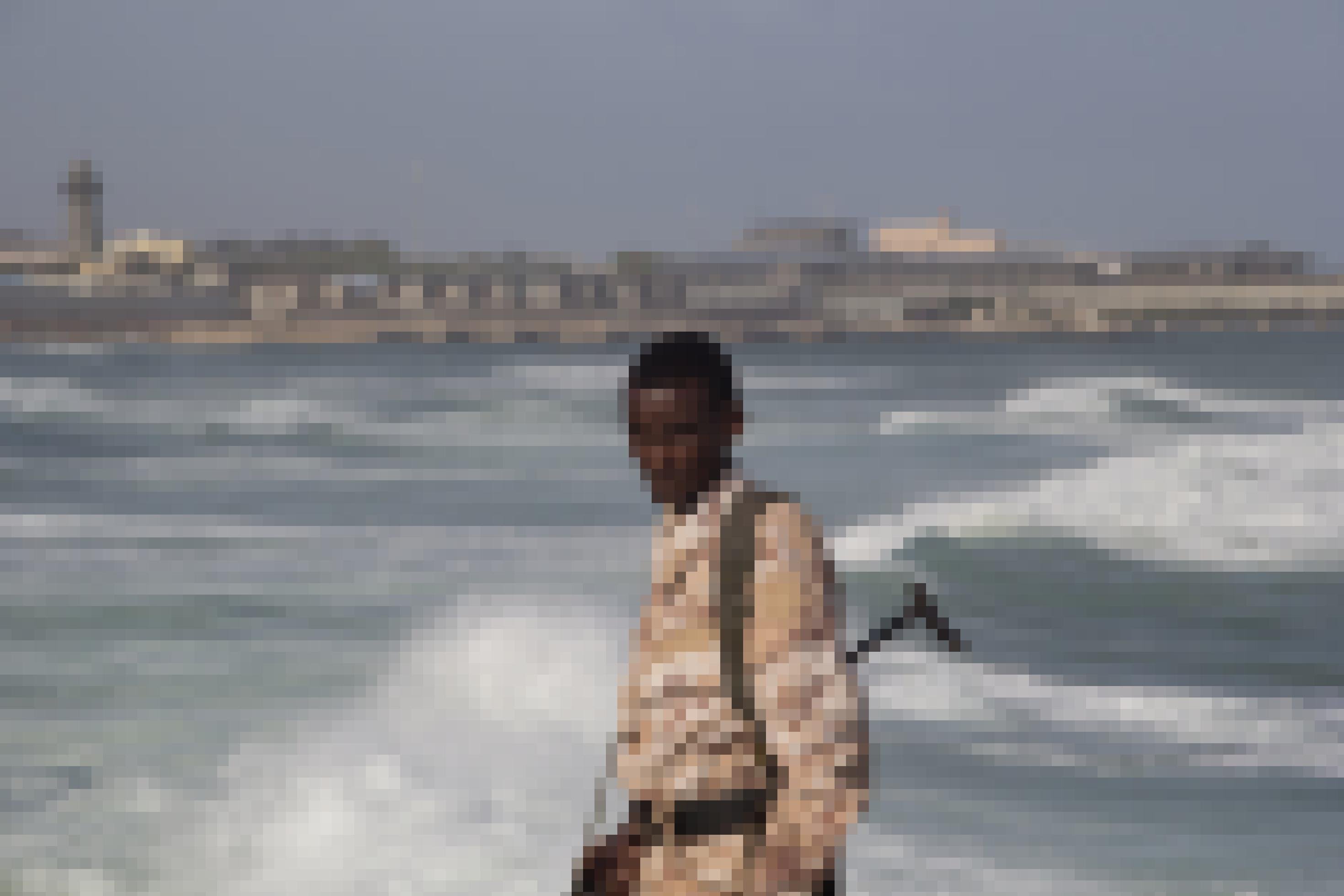 Ein Mann in Wüsten-Flecktarn und einem Gewehr steht an einem Strand.