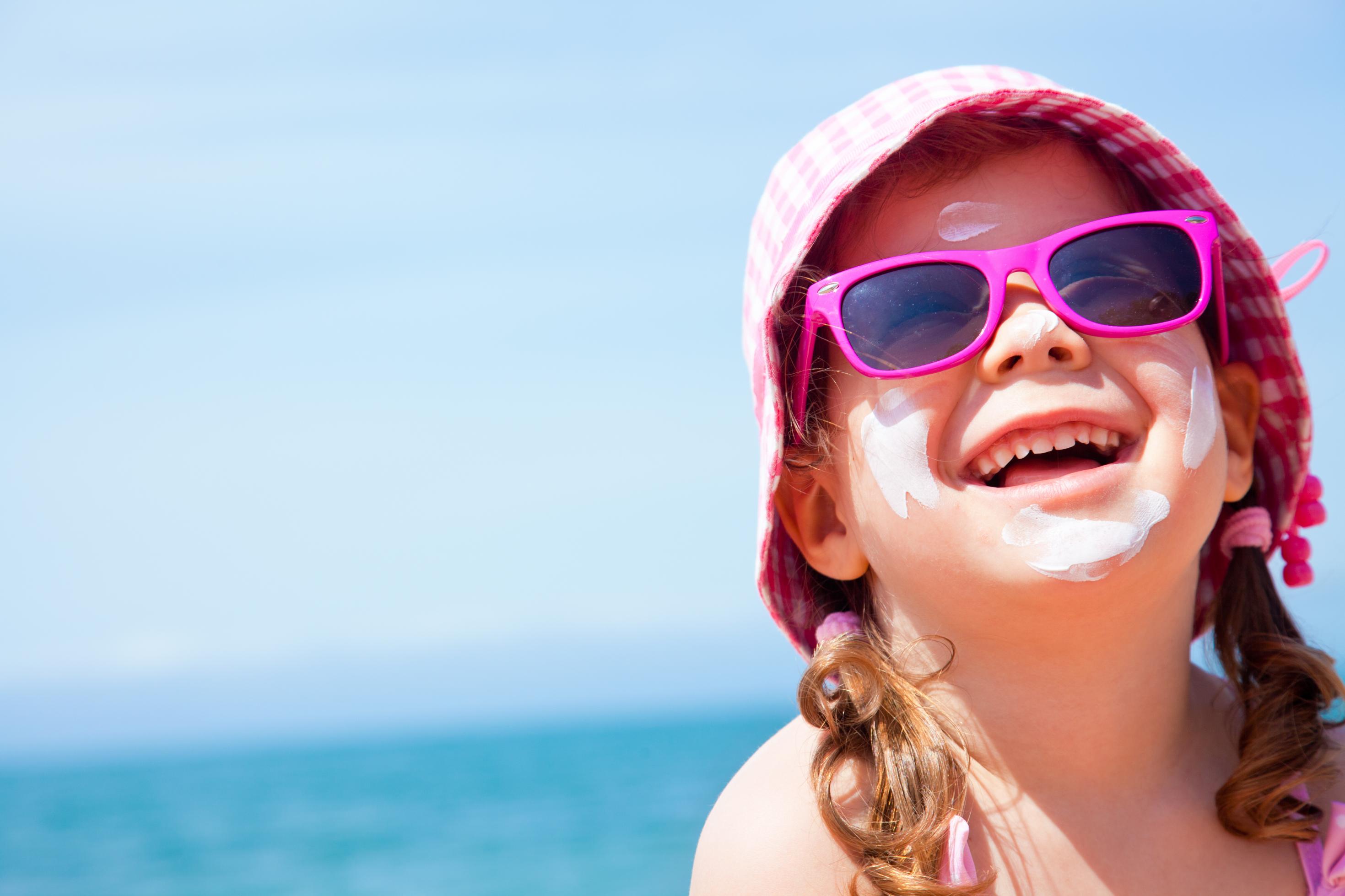 Ein kleines Mädchen mit pinker Sonnenbrille und weißen Sonnencreme-Flecken im Gesicht blickt in die Kamera. Sonnenschutzmittel müssen dick aufgetragen werden, um den angegebenen Lichtschutzfaktor zu erreichen.