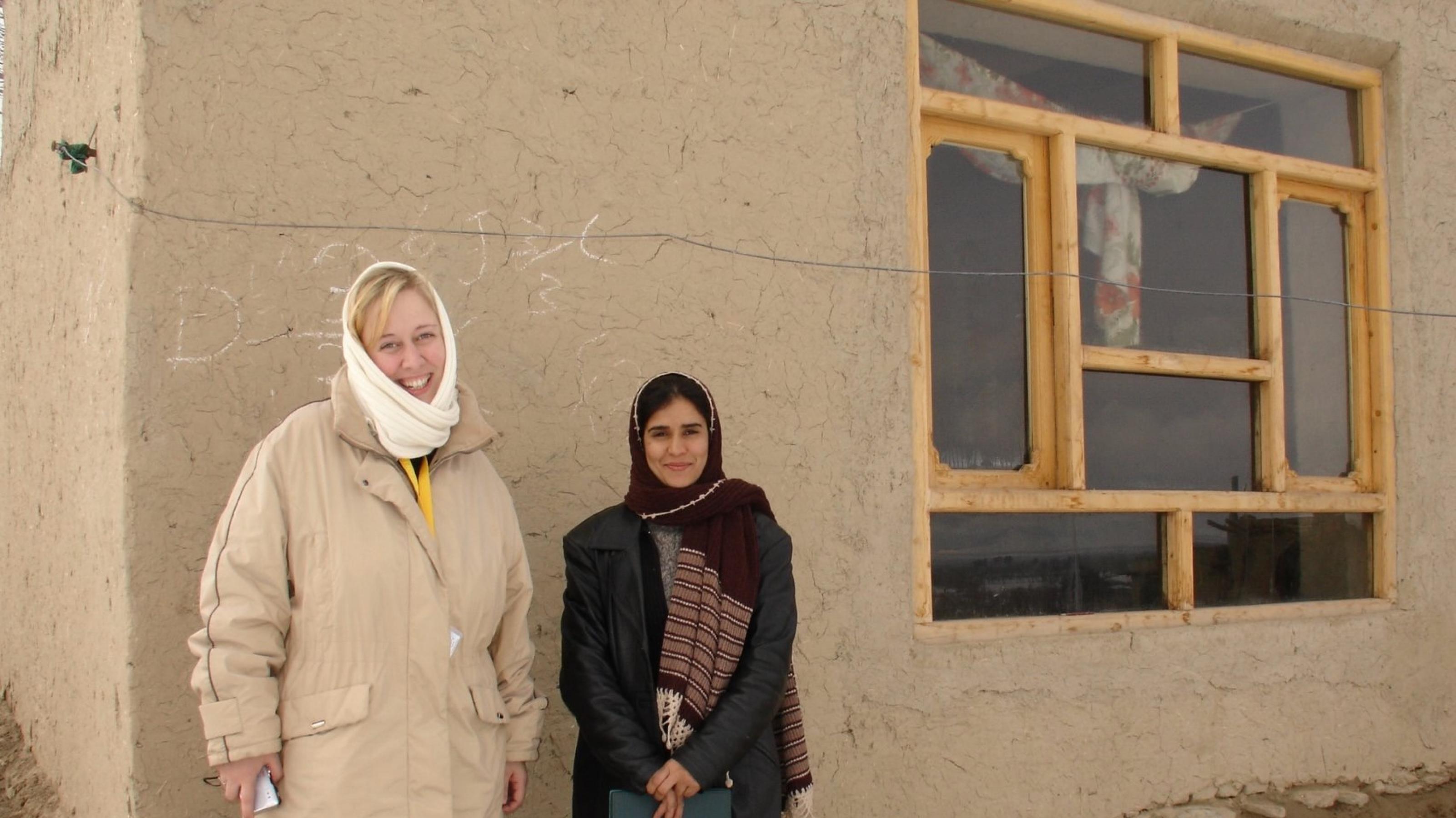 Die Journalistin Sonya Winterberg steht in Skikleidung vor einem Lehmhaus in Afghanistan mit einer afghanischen Architektin.