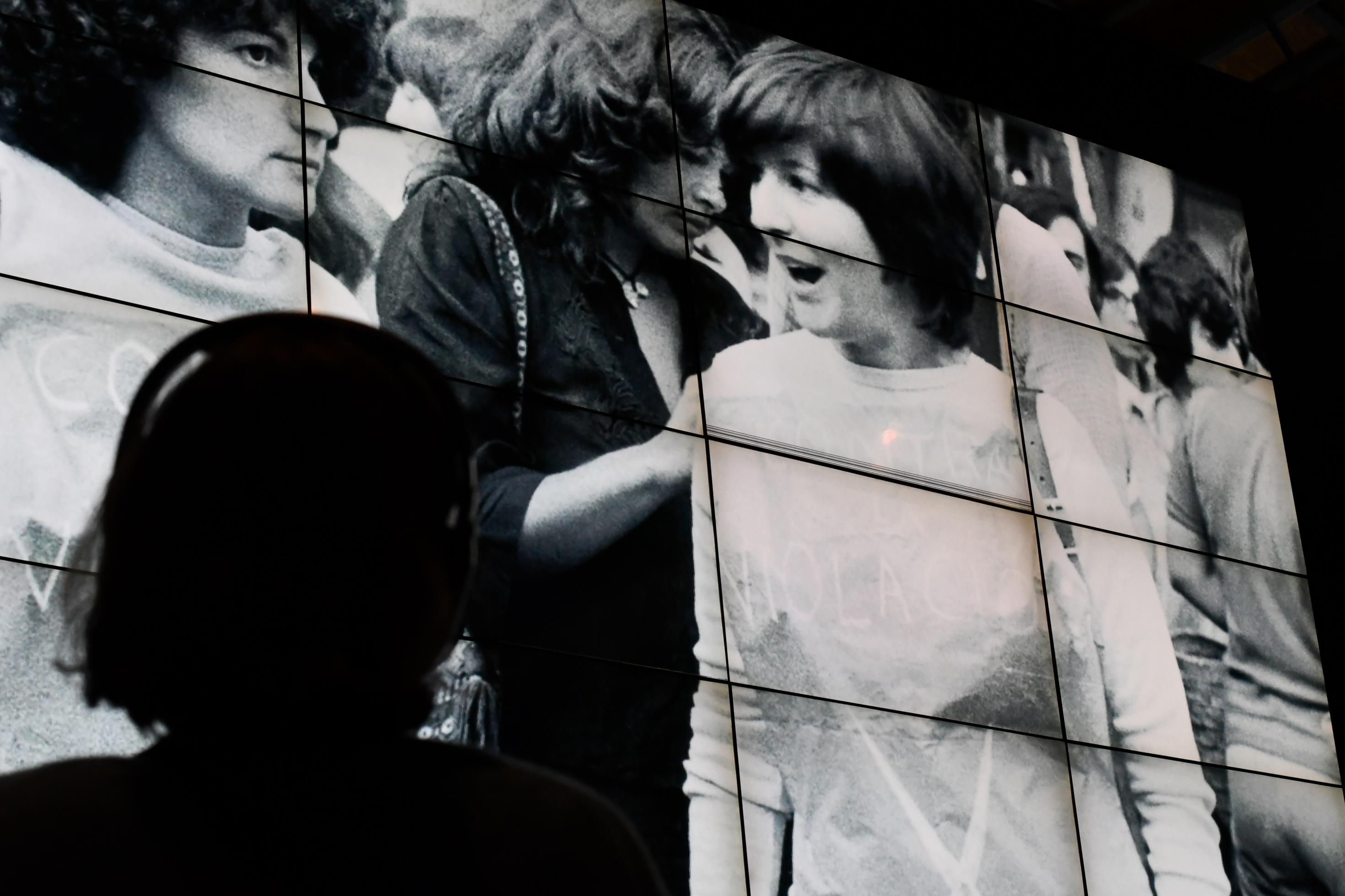 Auf einem großen Screen sind Fotos von demonstrierenden Frauen in den 1970er Jahren in Spanien zu sehen. Davor steht eine Betrachterin mit Kopfhörern.