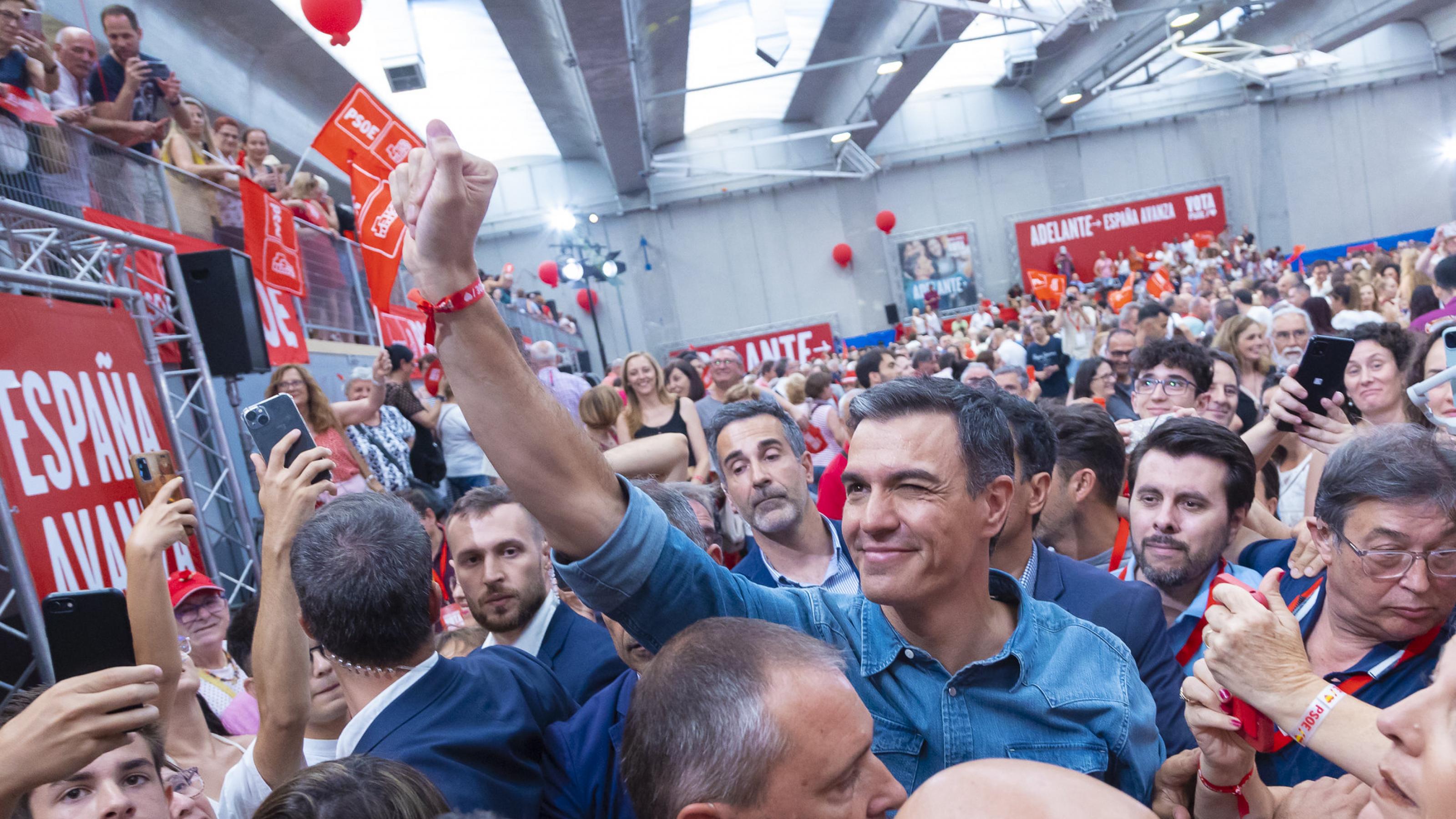 Der spanische Premier Pedro Sánchez steht in einer Menschenmenge und reckt die rechte Faust nach oben. Im Hintergrund ist der Wahlkampfslogan „Adelante“ („Vorwärts“) zu sehen