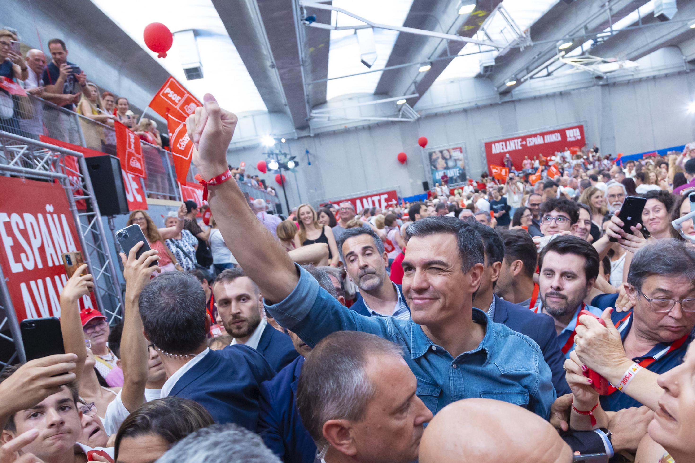 Der spanische Premier Pedro Sánchez steht in einer Menschenmenge und reckt die rechte Faust nach oben. Im Hintergrund ist der Wahlkampfslogan „Adelante“ („Vorwärts“) zu sehen