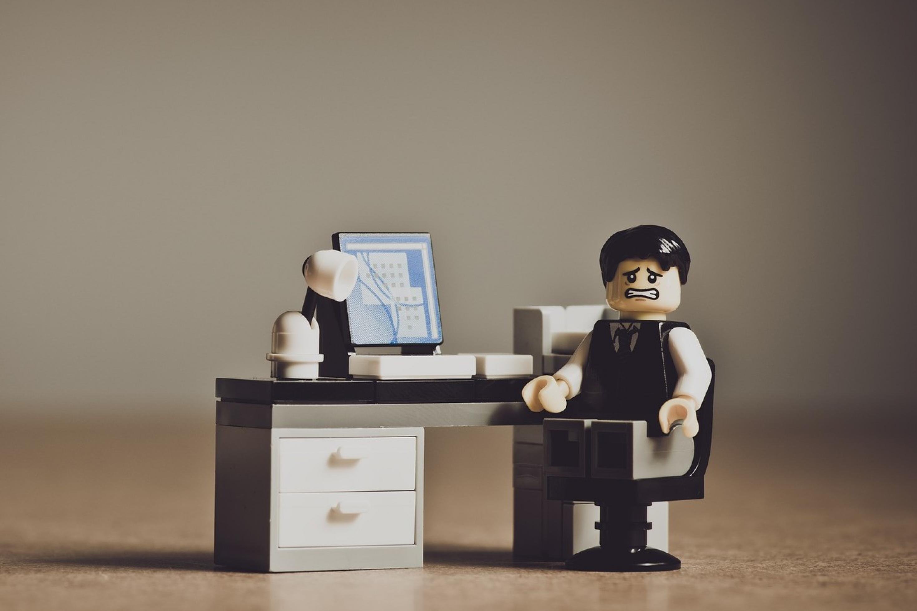 Ein Lego-Männchen sitzt mit besorgtem, verängstigtem Gesichtsausdruck an einem Schreibtisch.