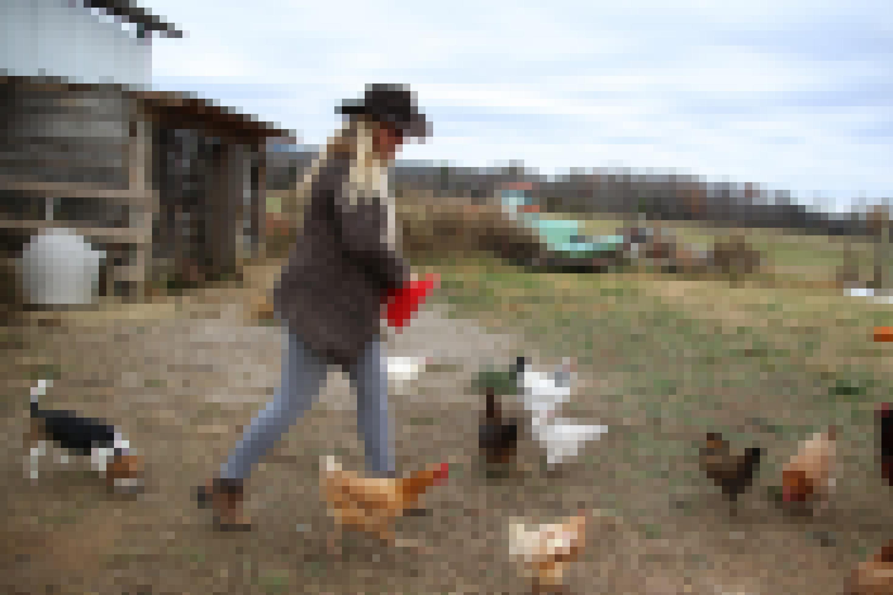 Eine junge Frau mit Cowboyhut füttert Hühner