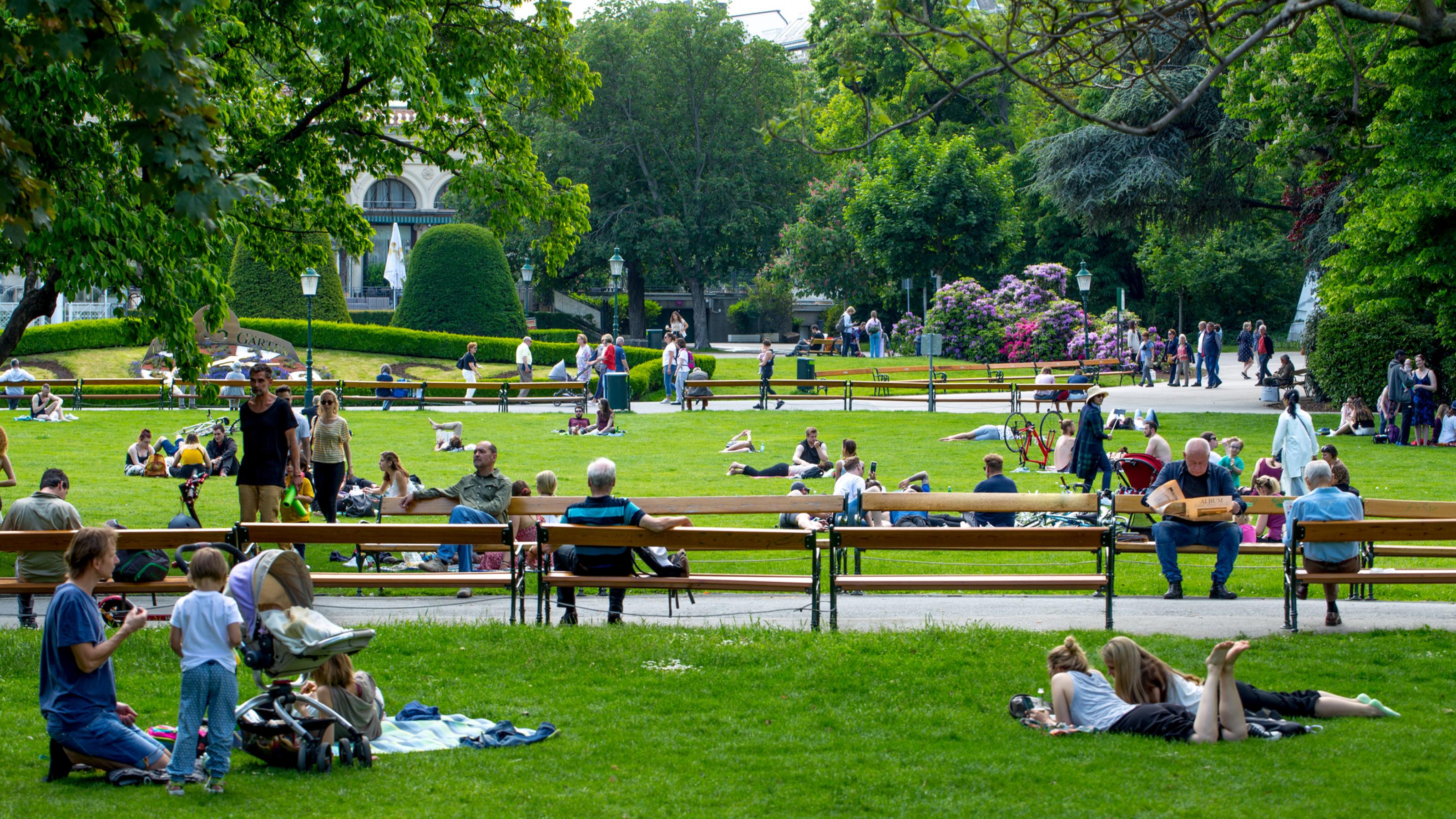 Menschen entspannen sich im kühlen Stadtpark in Wien an einem sonnigen, warmen Tag.
