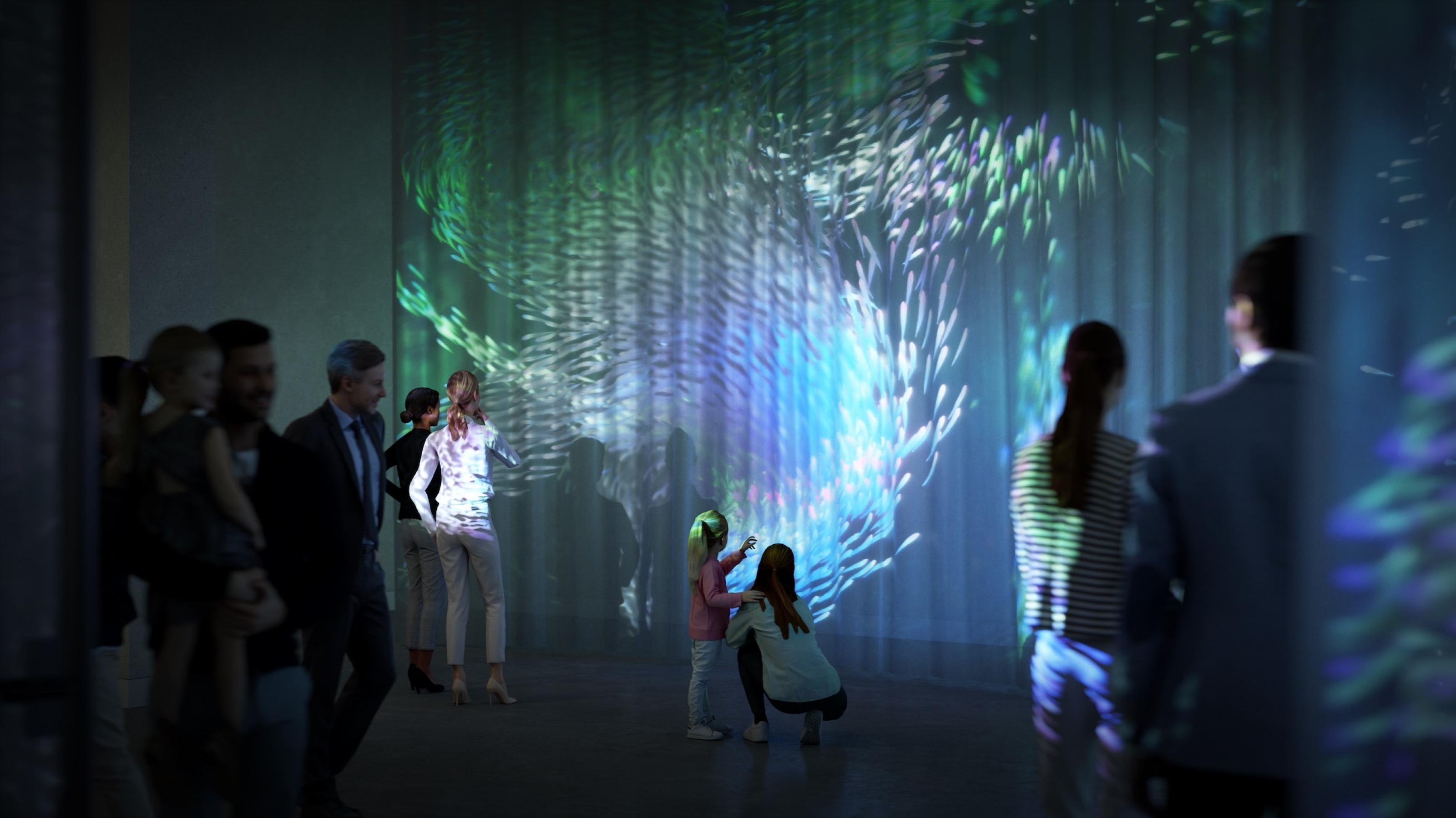 Das Bild zeigt den Entwurf eines Ausstellungsraums von „Nach der Natur“. Menschen stehen vor einer Projektion mit Fischen und abstrakten organischen Formen.
