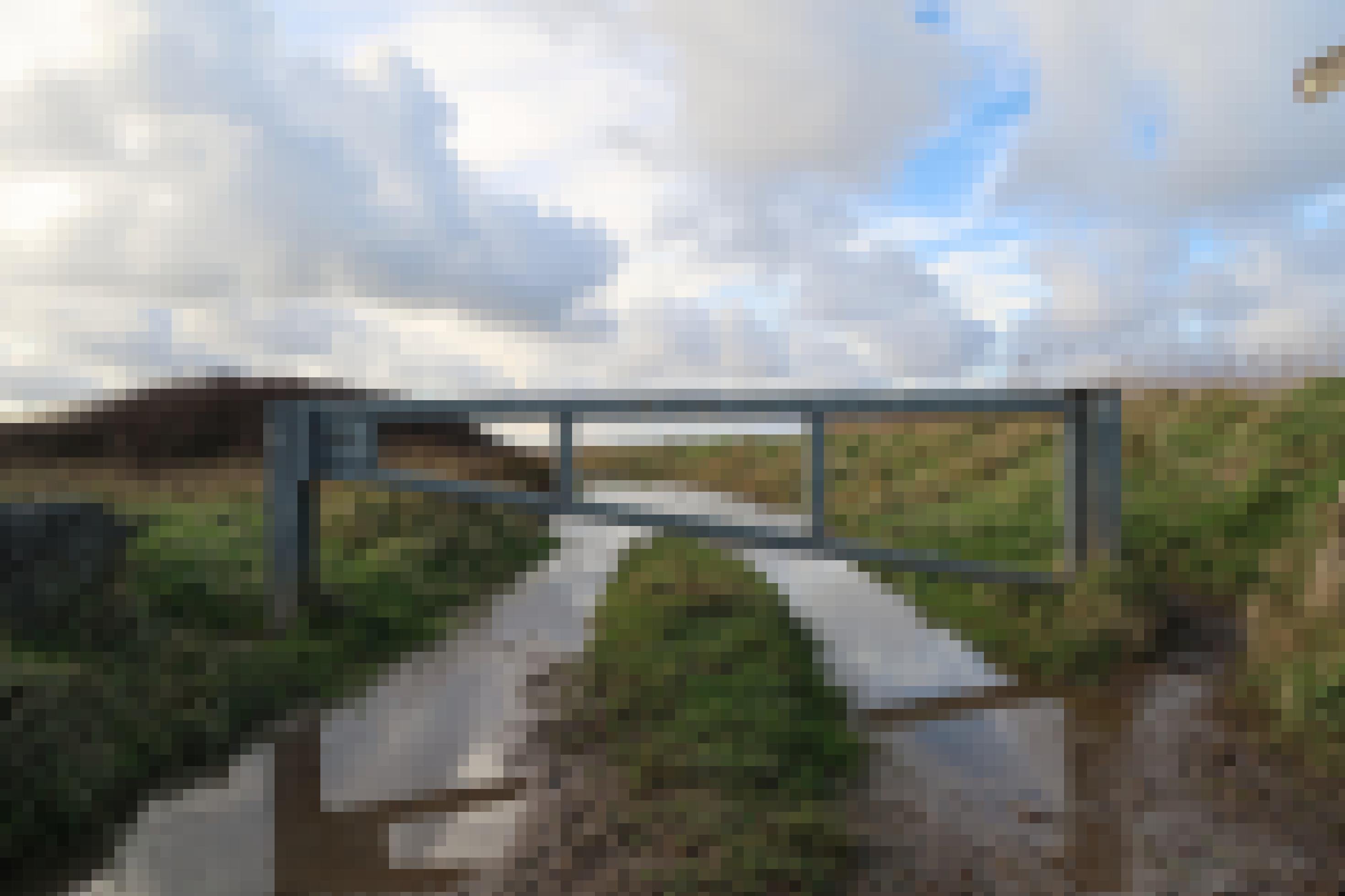 Hinter einer Schranke zeichnet sich ein überfluteter Feldweg ab