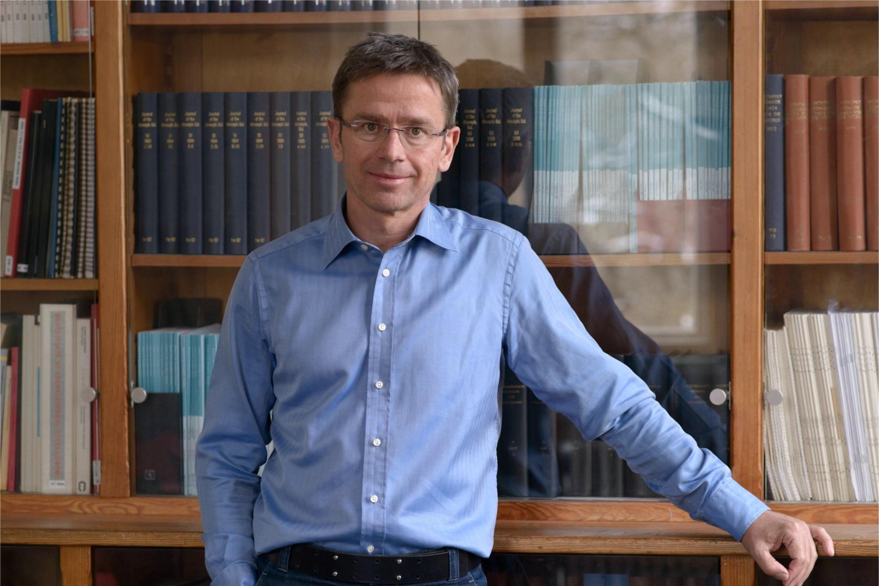 Professor Stefan Rahmstorf steht vor einem Bücherschrank. Er ist Klima- und Meeresforscher und leitet die Abteilung Erdsystemanalyse am Potsdam-Institut für Klimafolgenforschung (PIK).