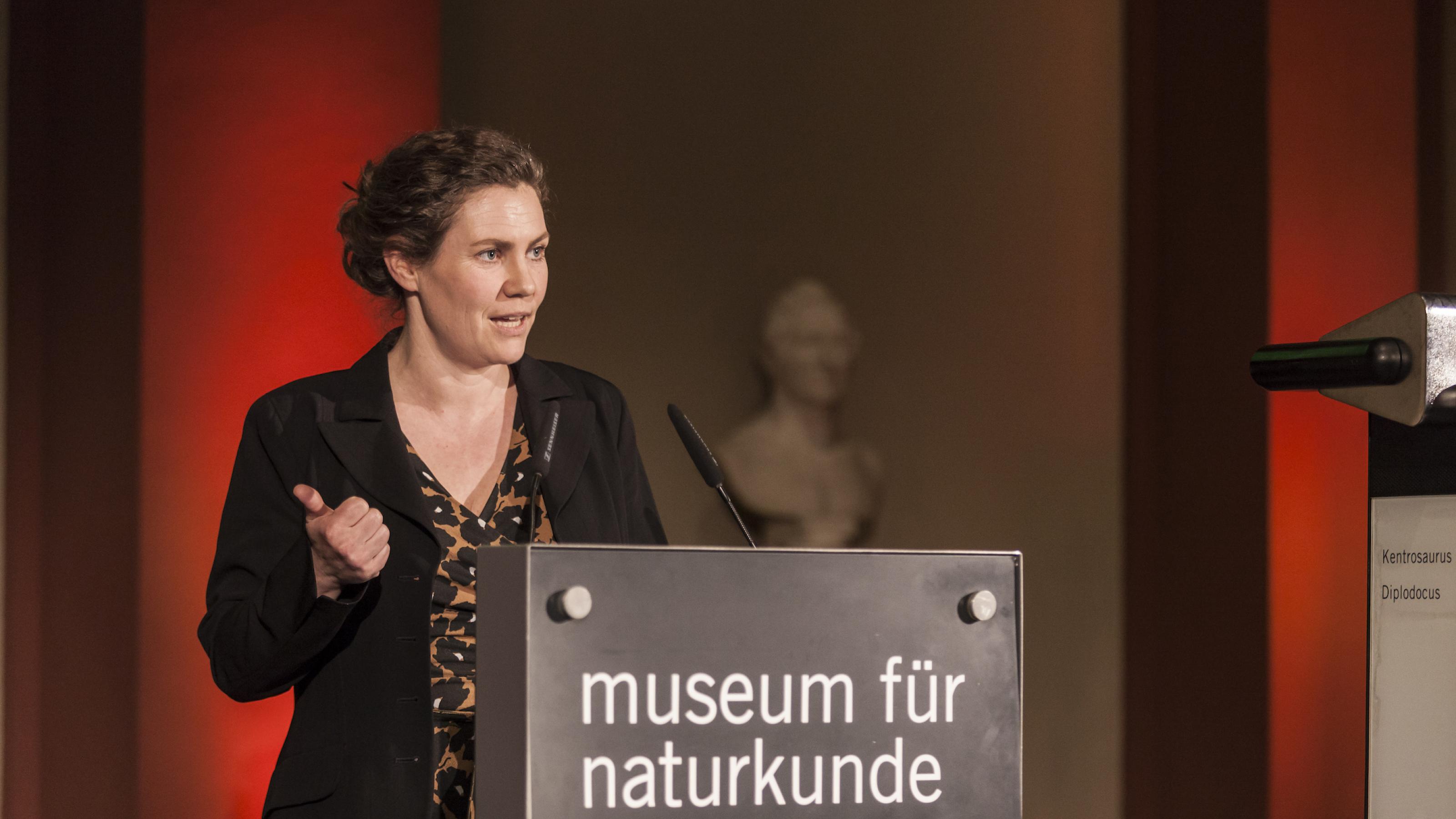 Eine Frau am Rednerpult, auf dem „Museum für Naturkunde“ steht.