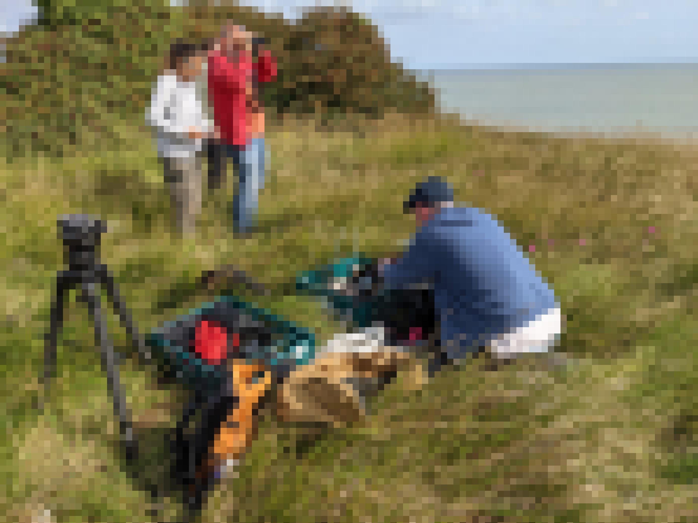 Ein Mann im Kapuzenpulli kauert im Gras um eine Kiste mit elektronischem Zubehör