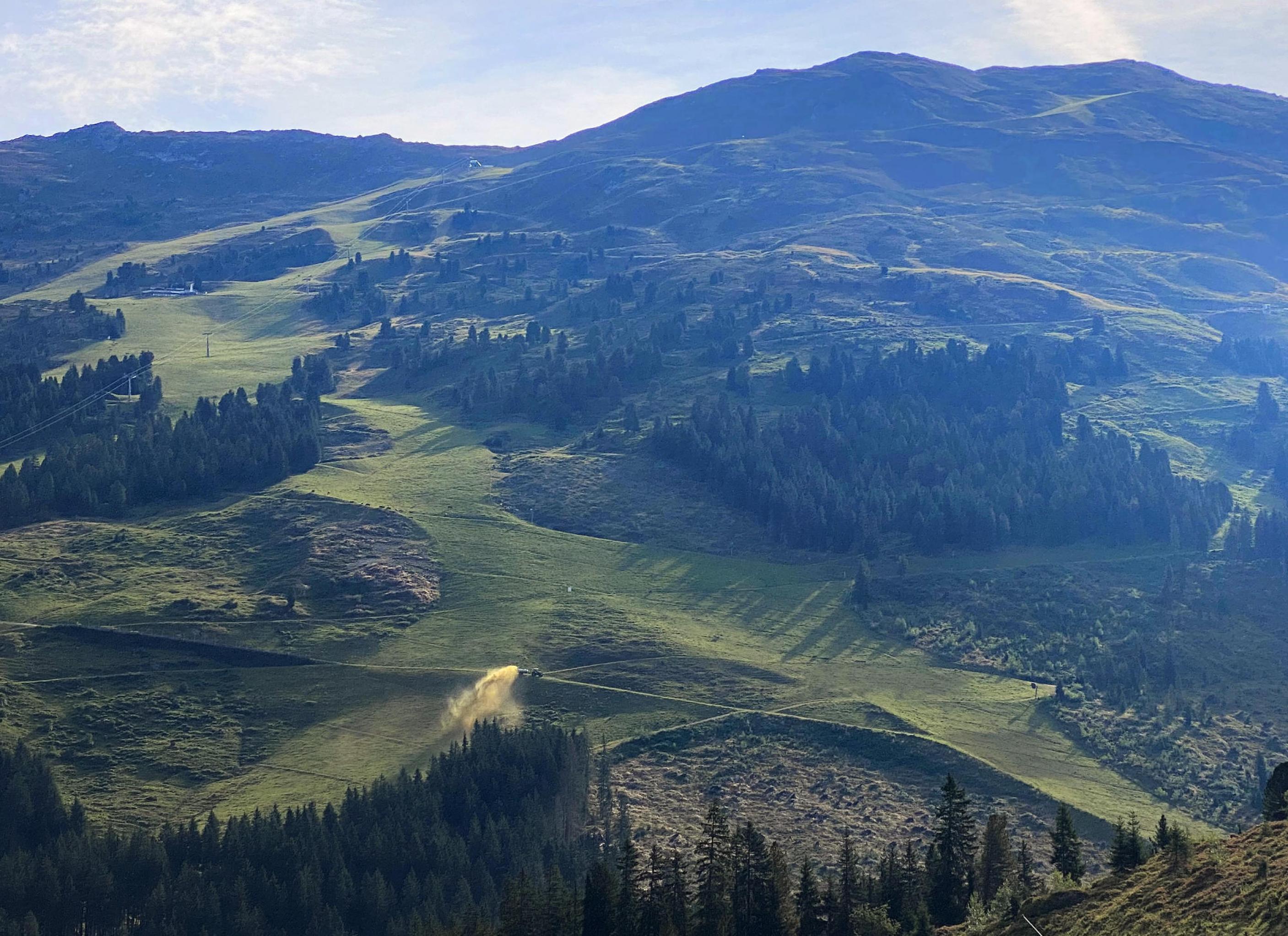 An einem Hang in den Bergen versprüht eine Landmaschine in hohem Bogen eine Düngerwolke.