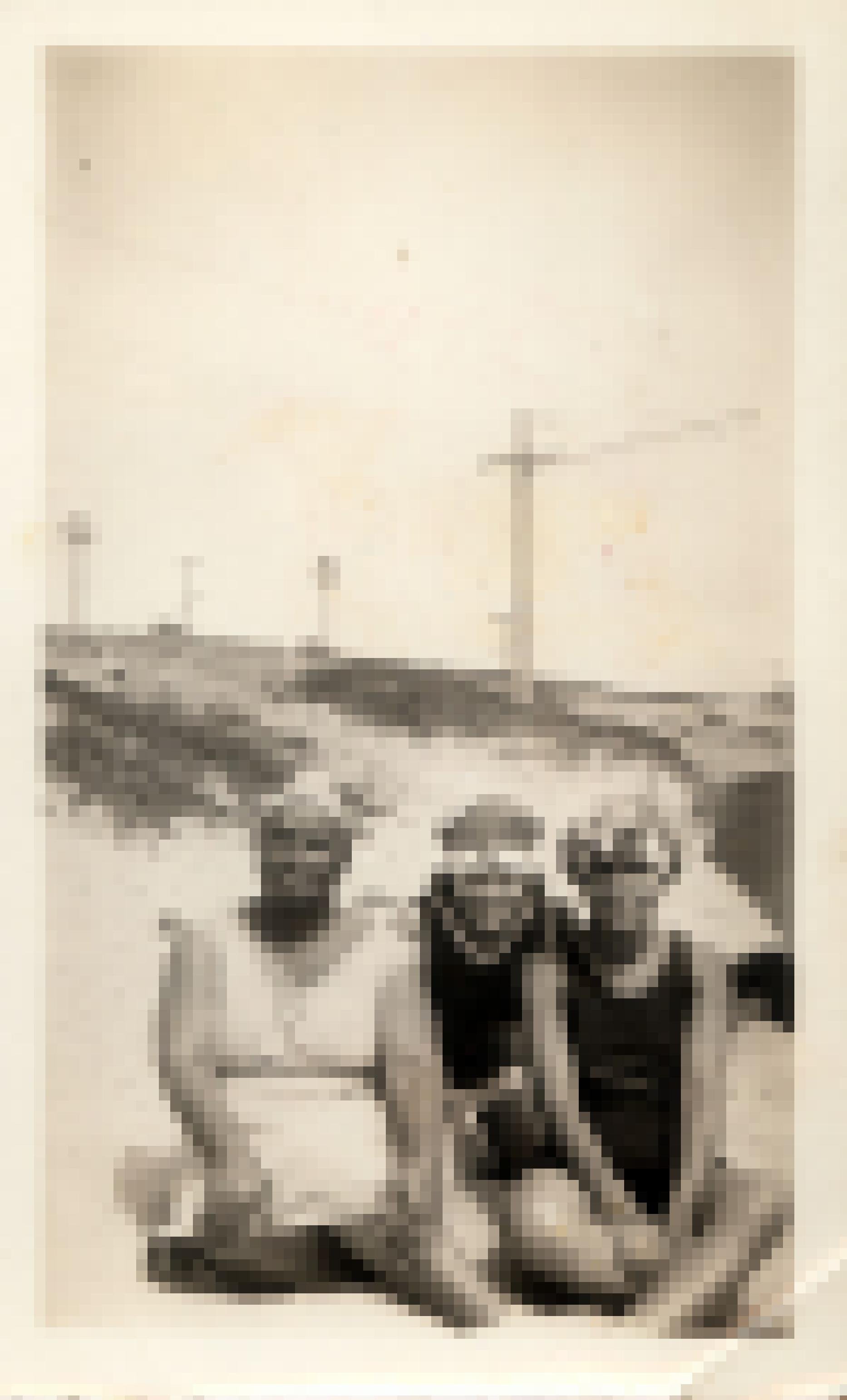 Drei Schwarze Frauen sitzen eng zusammen am Strand, schauen in die Kamera. Sie tragen Badekleidung und Badekappen im Stil der 1920er Jahre. Hinter ihnen eine Düne und Strommasten