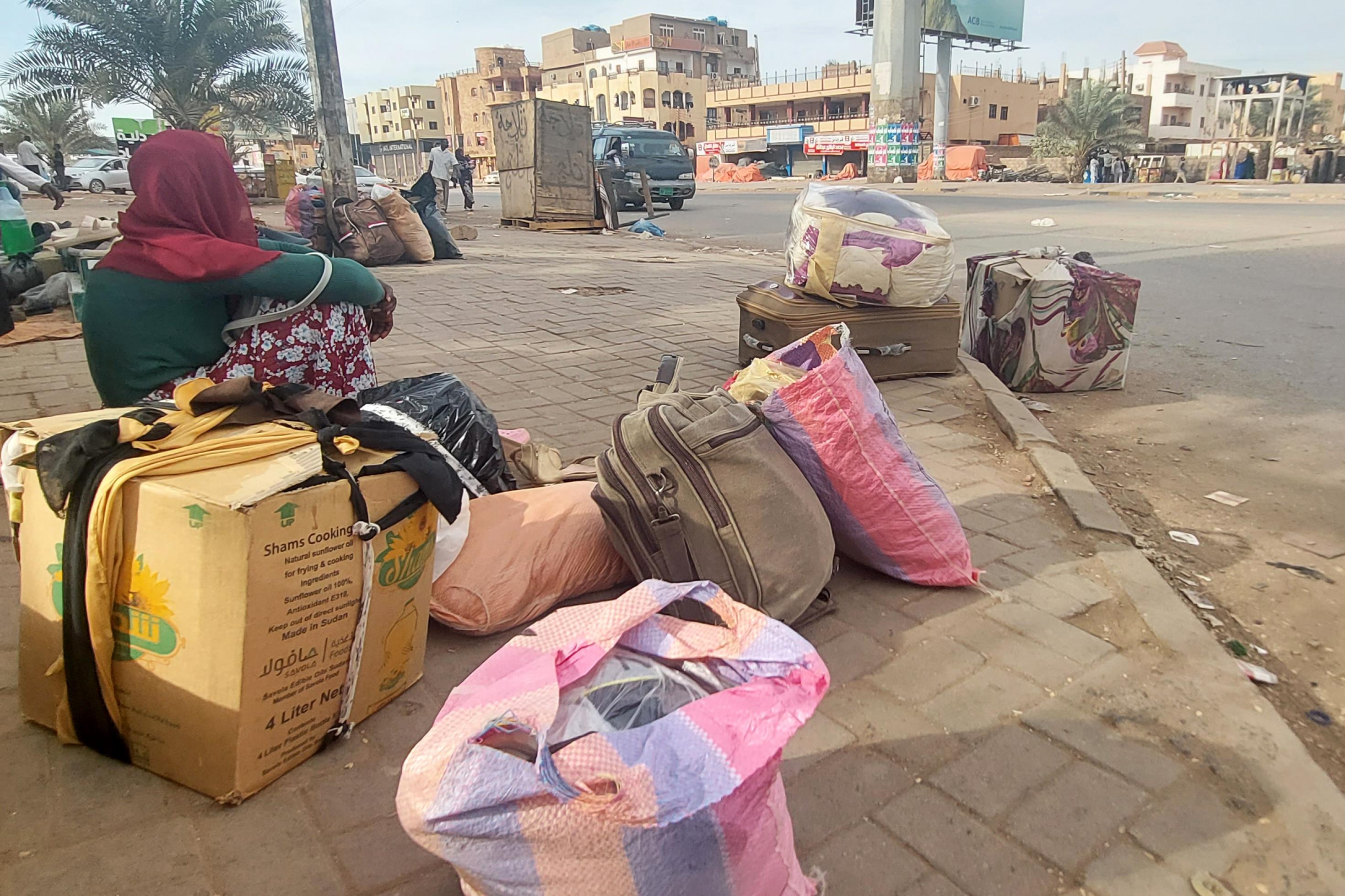Eine Frau auf einem Bürgersteig in der Hauptstadt Khartum, sie hat mehrere Gepäckstücke dabei.