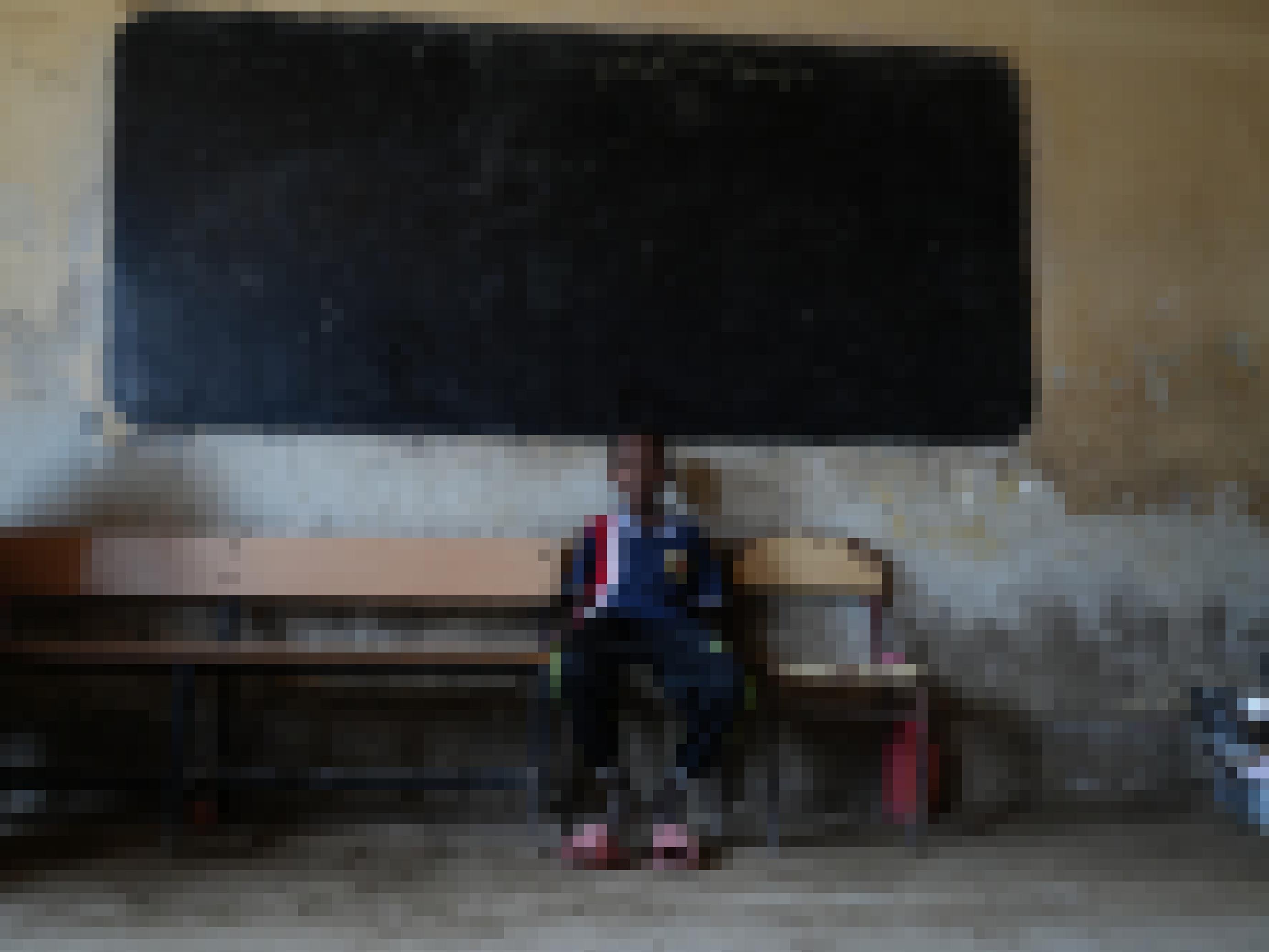 Ein schmächtiger Junge auf einer Bank vor einer Schultafel. Er sitzt womöglich in einem Klassenraum, in einem Schulgebäude, das nun für Vertriebene genutzt wird.
