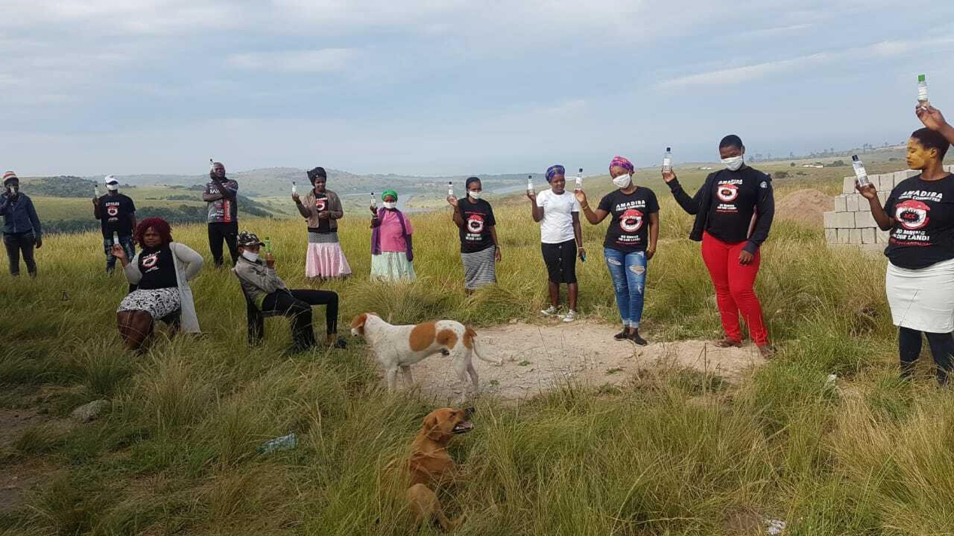 Südafrikanische Aktivisten des 'Amadiba Crisis Committee" stehen auf einem Hügel der ländlichen Transkei in Südafrika und halten Fläschen mit Handdesinfektionsmitteln hoch.