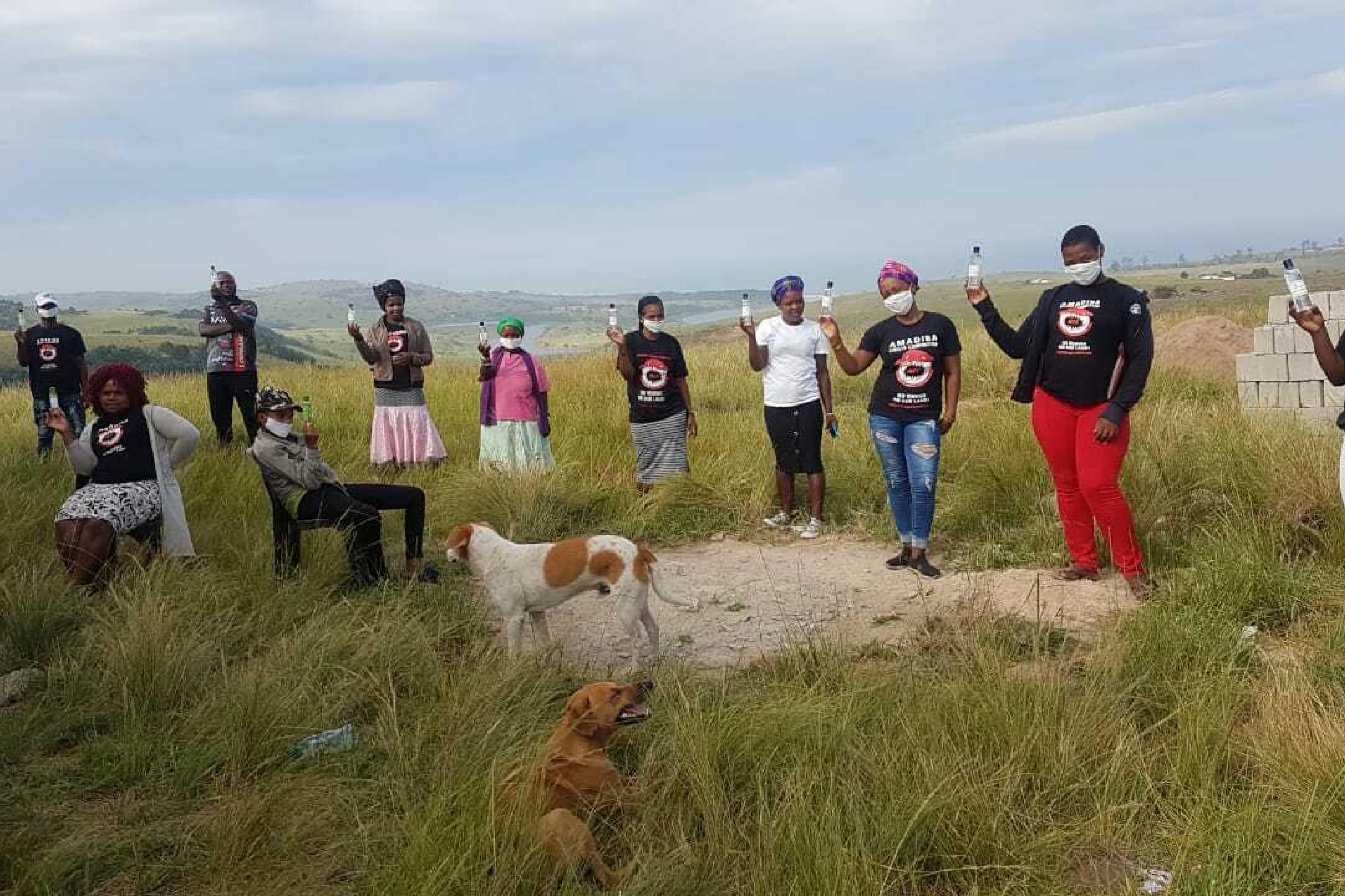 Südafrikanische Aktivisten des 'Amadiba Crisis Committee" stehen auf einem Hügel der ländlichen Transkei in Südafrika und halten Fläschen mit Handdesinfektionsmitteln hoch.