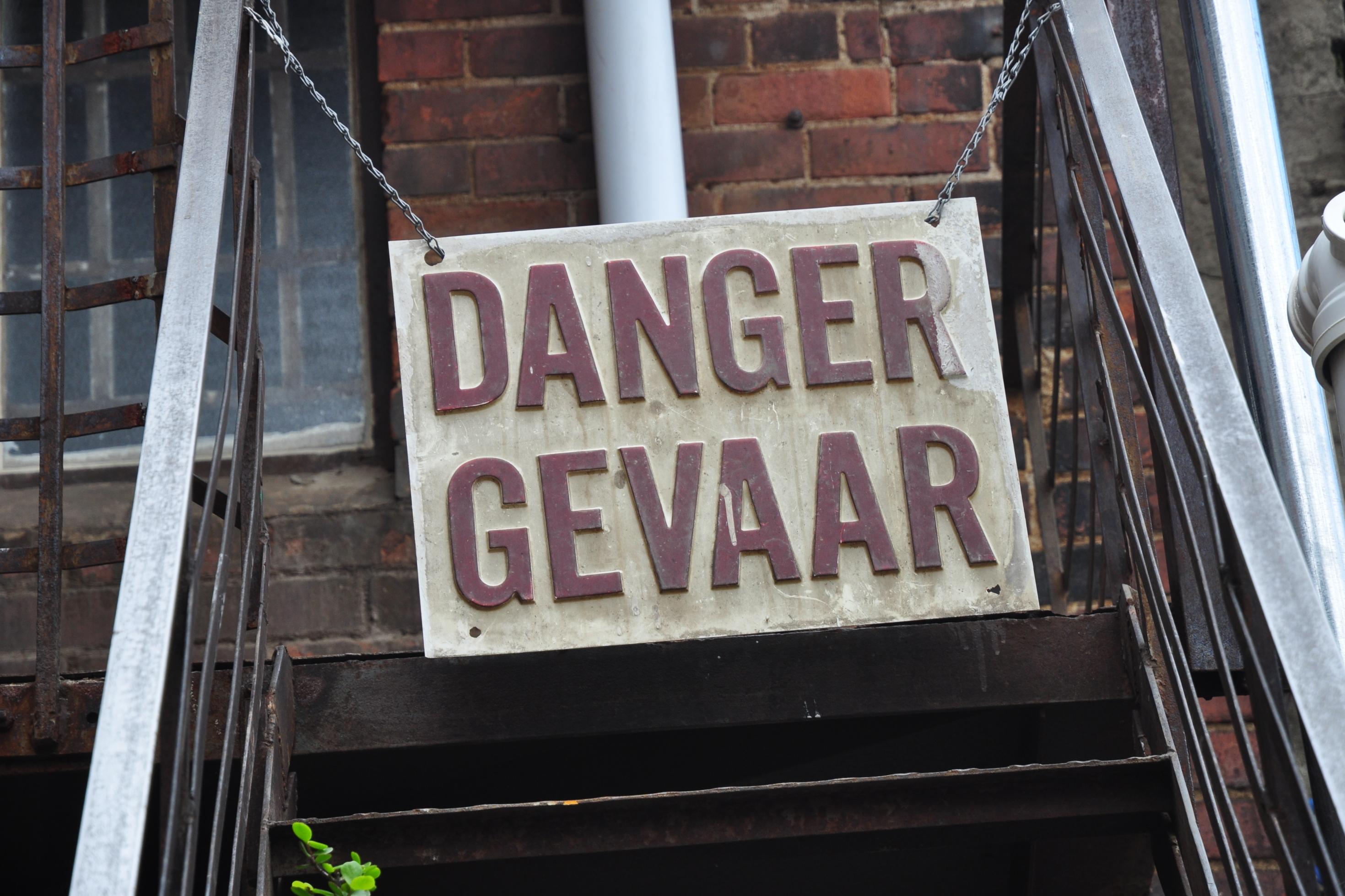 Das Foto zeigt ein Schild, das einen Treppenaufgang versperrt, mit der Aufschrift: Danger. Gefahr.