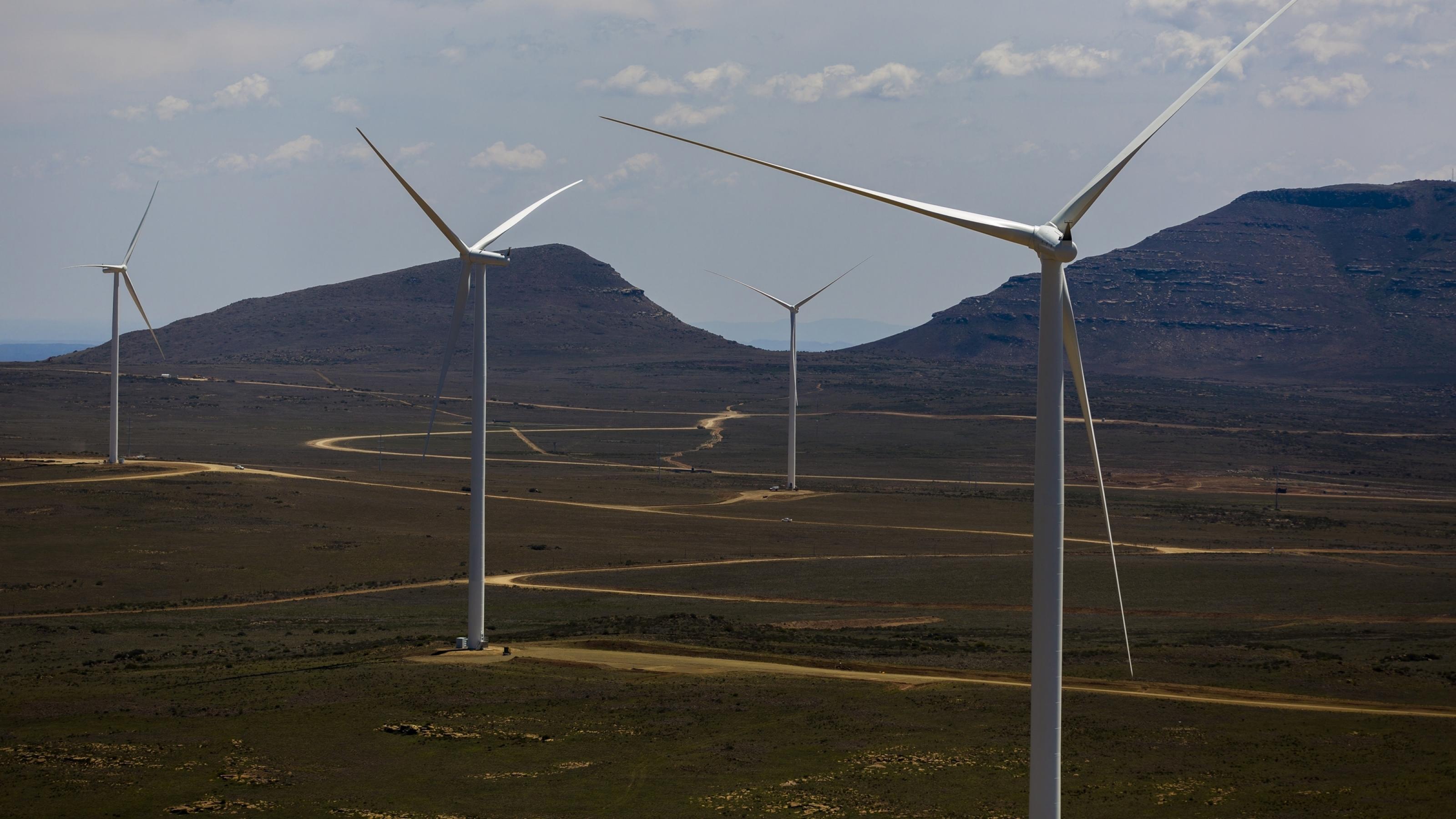 Eine Windfarm in Südafrika. Man sieht die Windanlagentürme und die Landschaft.