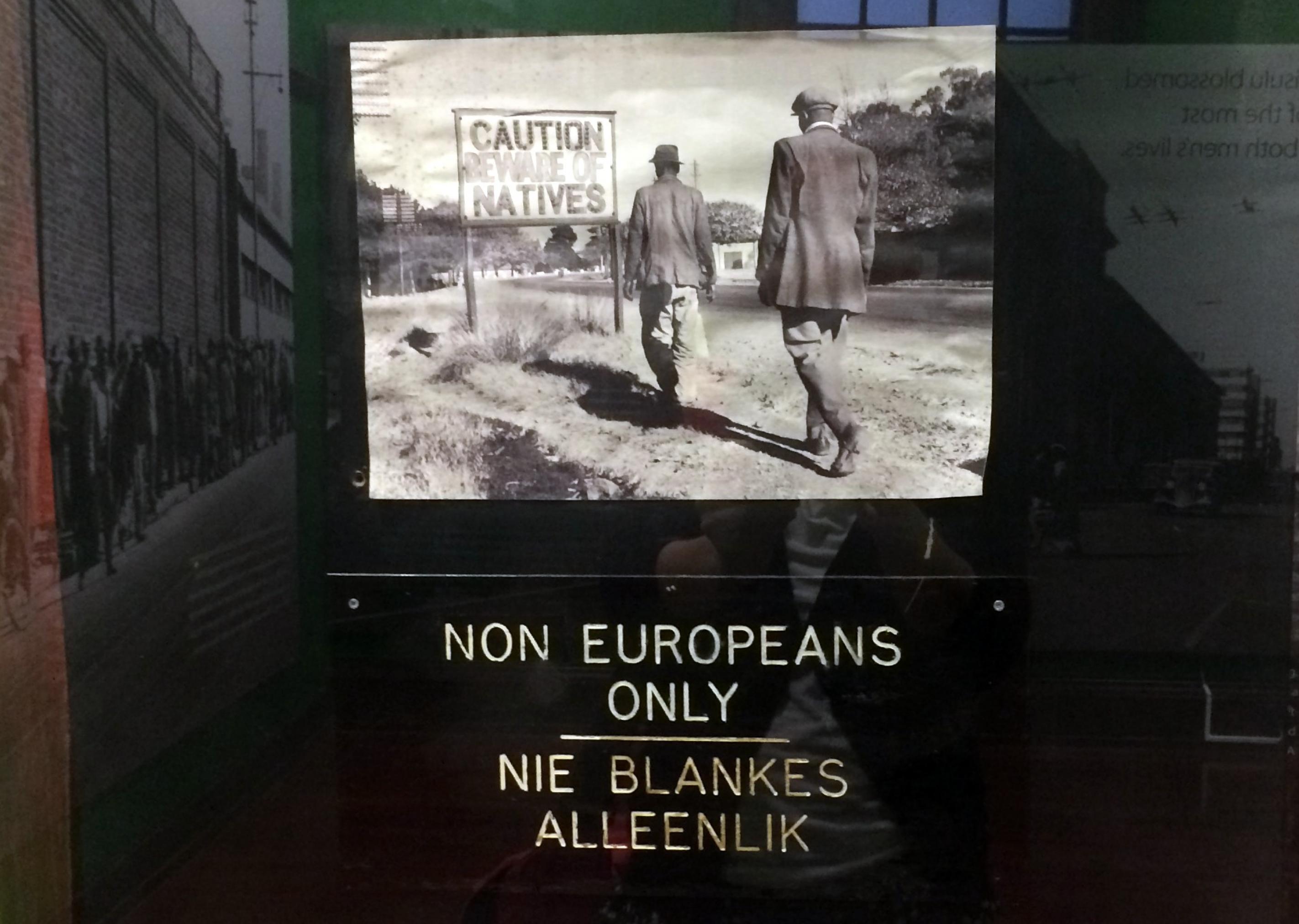 Ein Exponat im Mandela Museum zeigt den Alltag während der Apartheid, das Foto  zeigt zwei Männer die auf ein Schild mit der Aufschrift: Caution Natives, also Vorsicht Einheimische