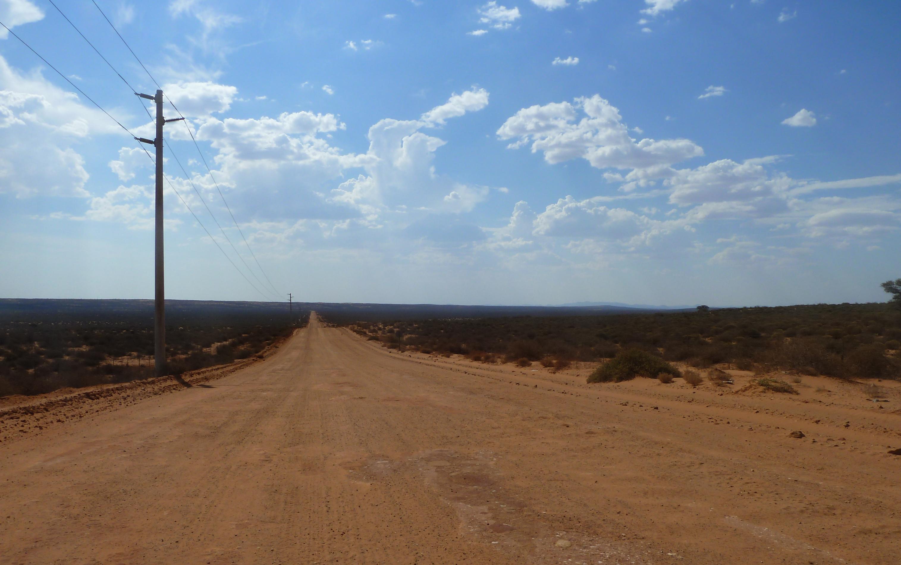 Eine leere rötliche Sandpiste in karger, menschenleerer Landschaft