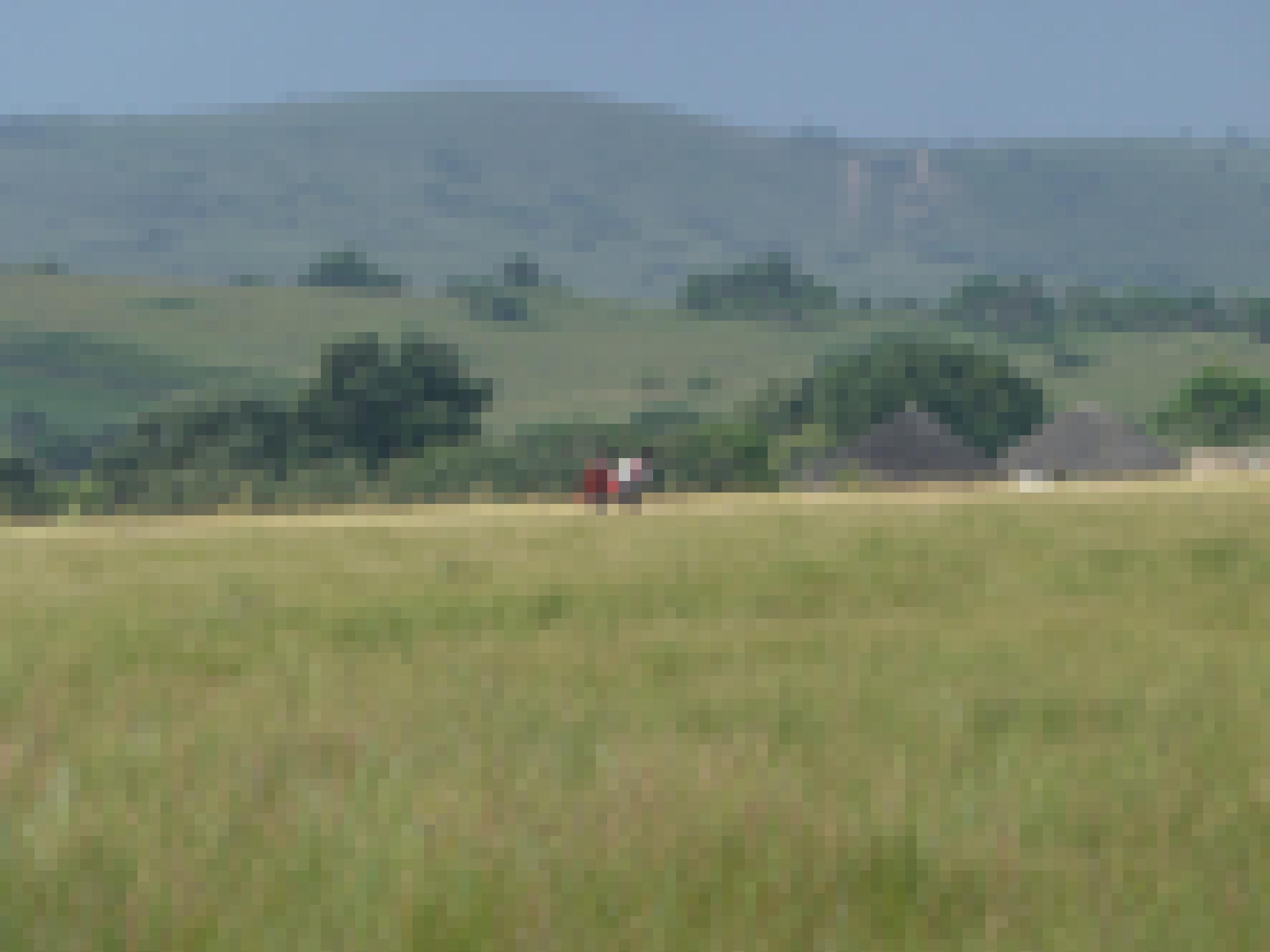 Inmitten der Hügellandschaft sind zwei Grundschüler auf dem Schulweg, sie gehen an zwei strohgedeckten Rundhütten vorbei.