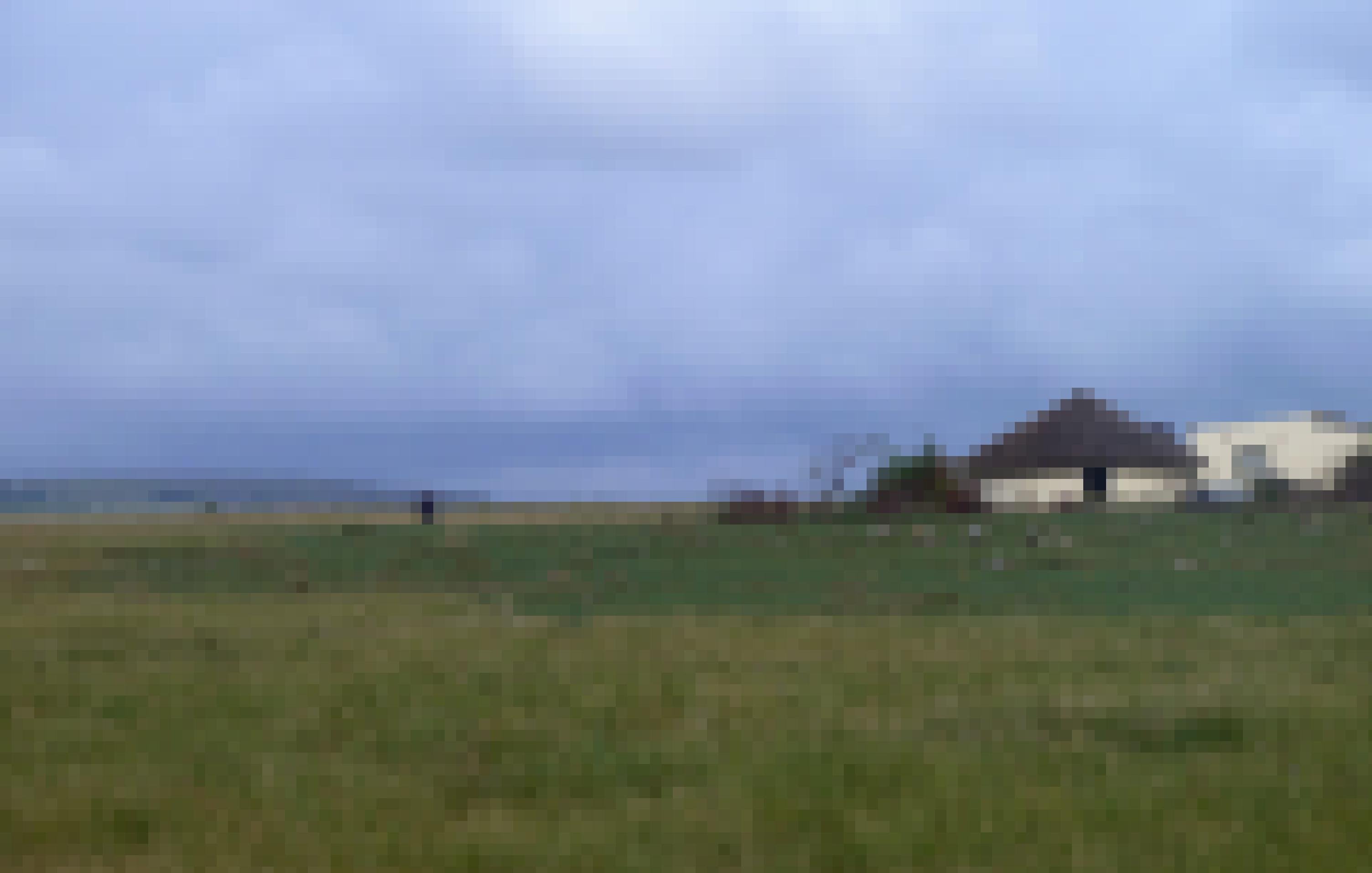 Zwei Kinder sind in einer großen Graslandschaft neben einem traditionellen Rundhaus zu sehen