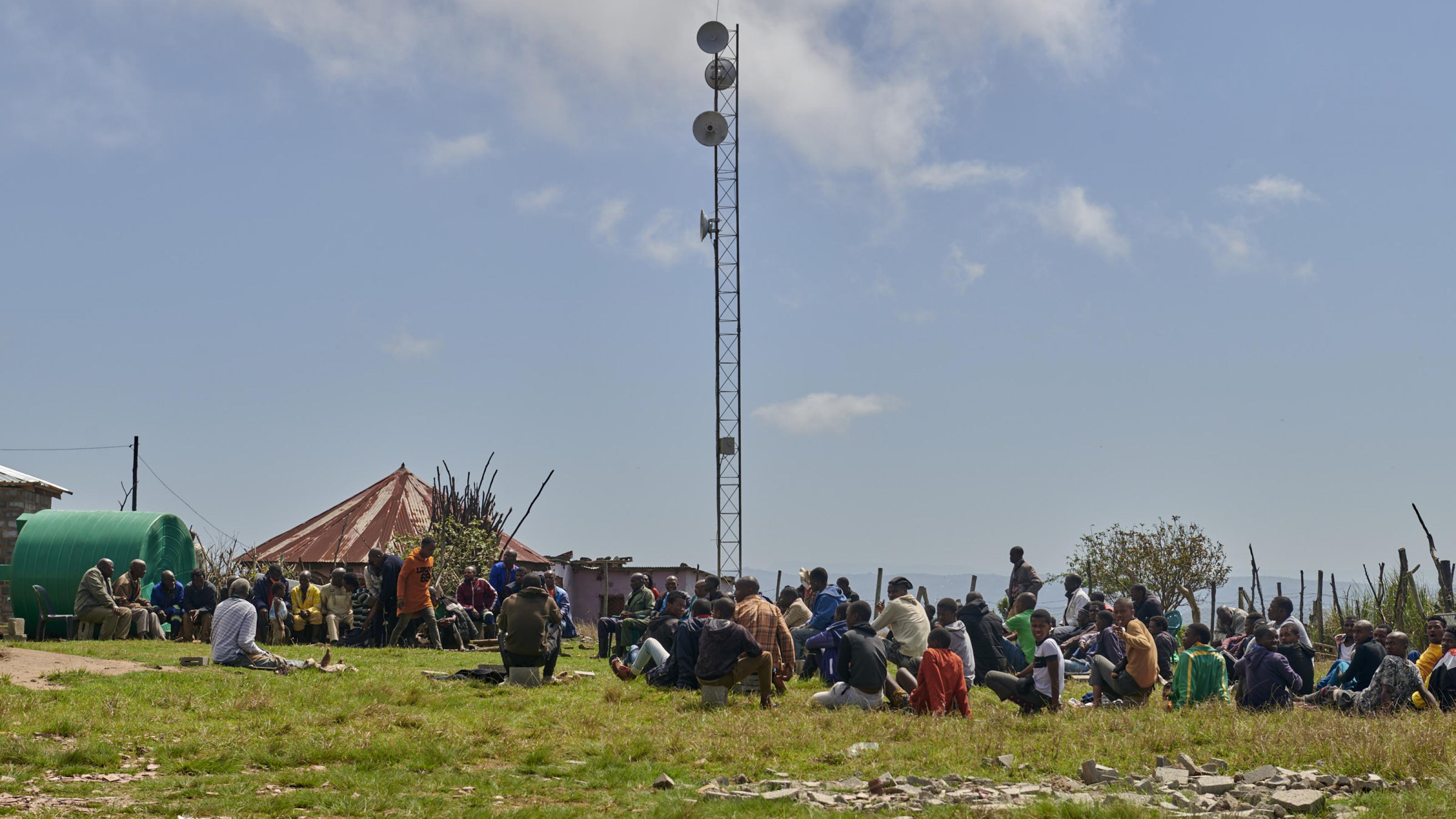 Der Mast des Netzwerks steht auf einem Grundstück mit einem Rundhaus, vor dem sich Dorfbewohner versammelt haben