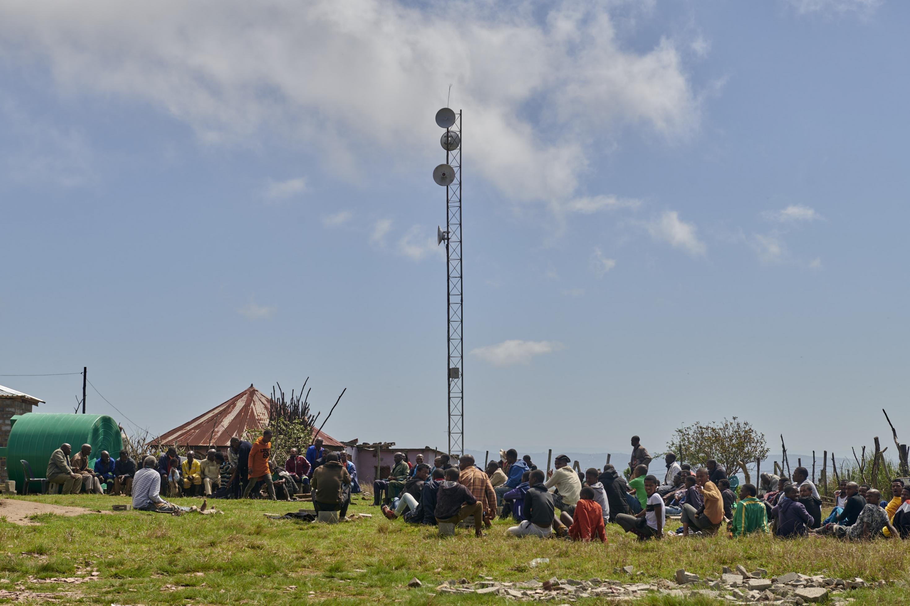 Der Mast des Netzwerks steht auf einem Grundstück mit einem Rundhaus, vor dem sich Dorfbewohner versammelt haben