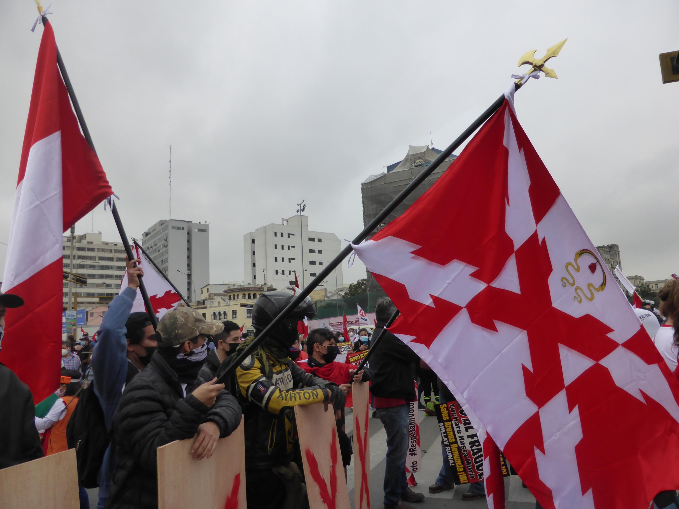 Demonstranten mit Fahnen, die ein quer gelegtes rotes Kreuz zeigen.