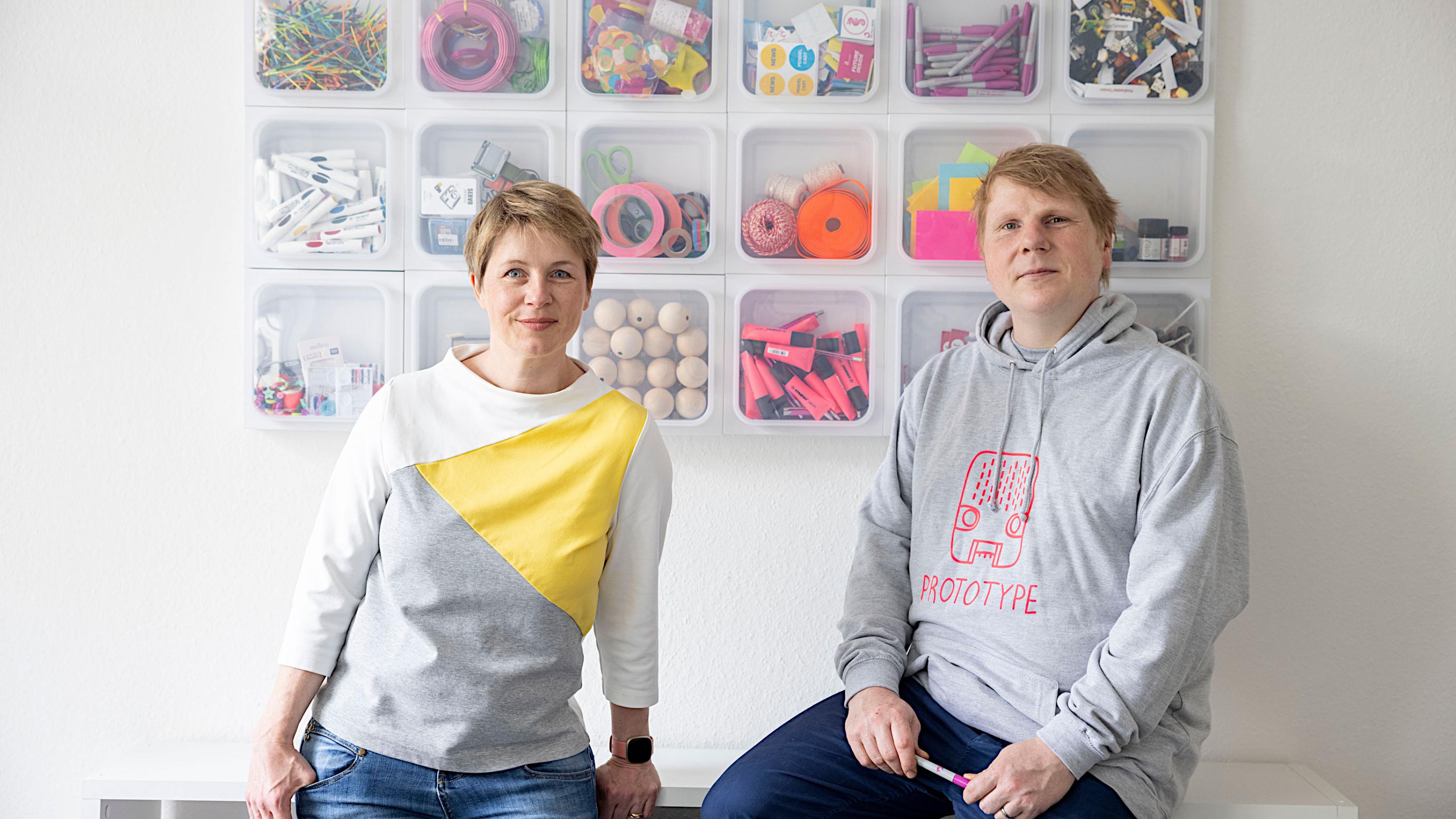 Astrid Csuraji und Jakob Vicari vor einer Wand mit Kreativmaterialien