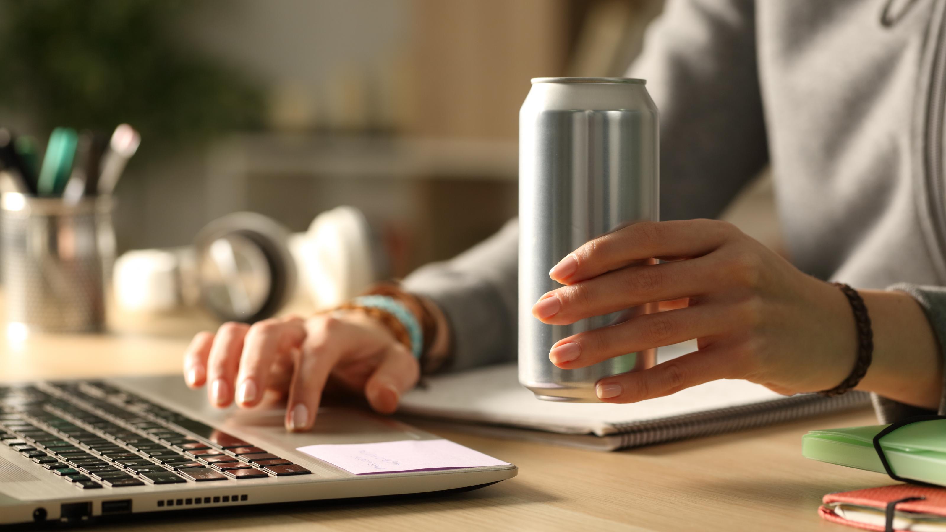 Großaufnahme von Frauenhänden mit Energy-Drink-Dose und Laptop auf dem Schreibtisch