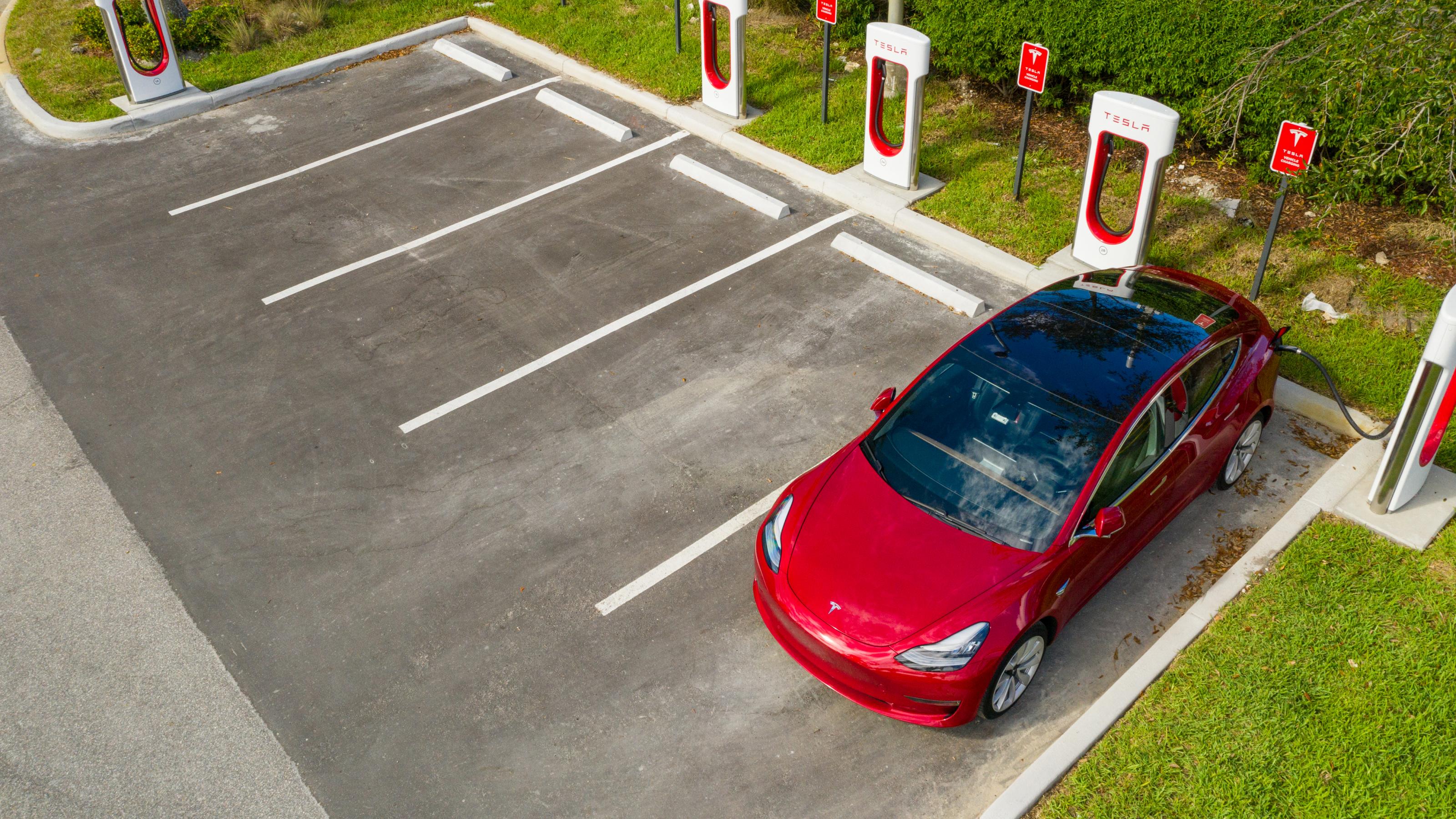 Luftbild eines roten Elektroautos, das an einer Tesla-Ladesäule hängt.