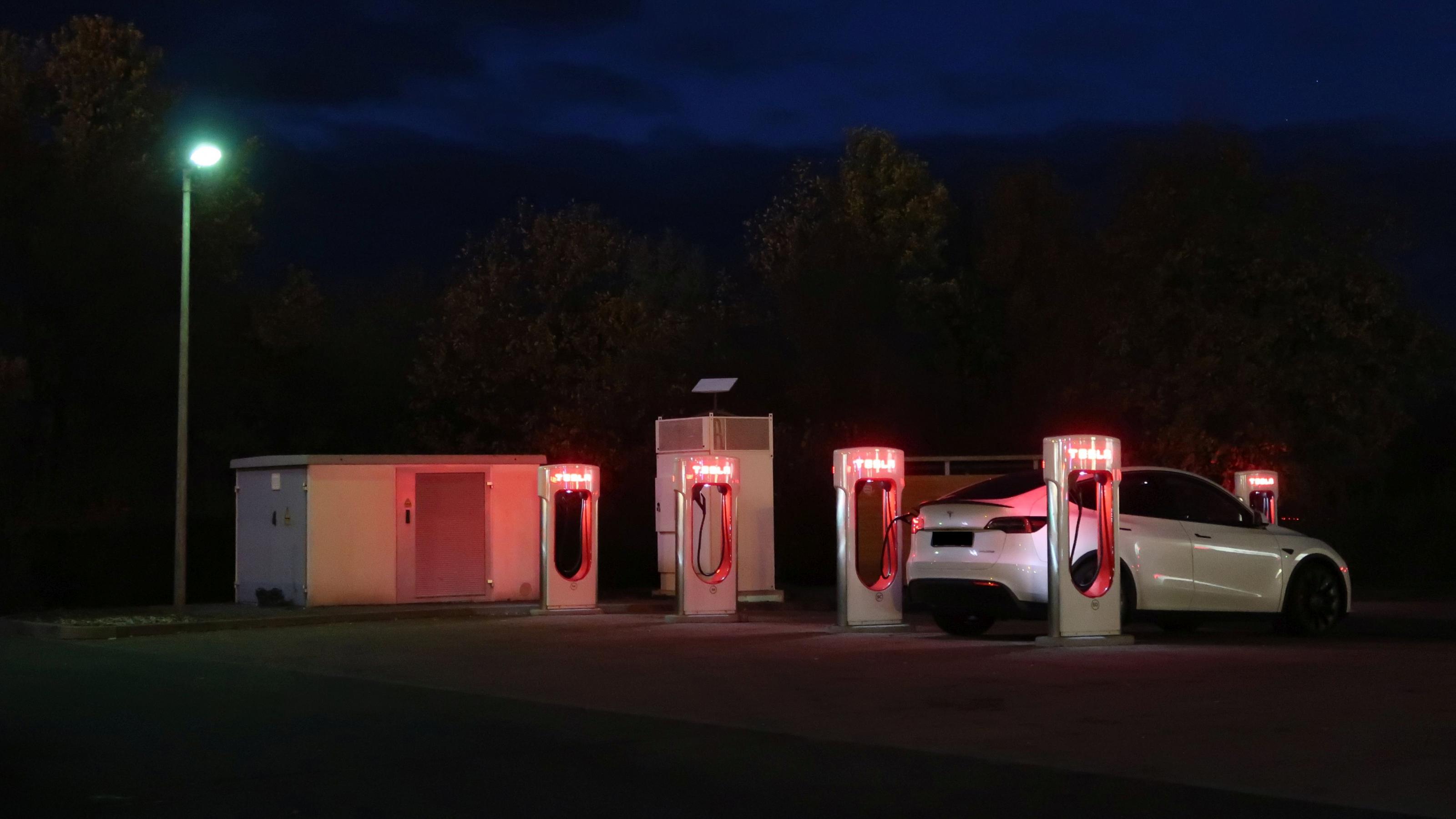 Elektroauto lädt Strom im Dunkeln an einem Tesla-Supercharger.