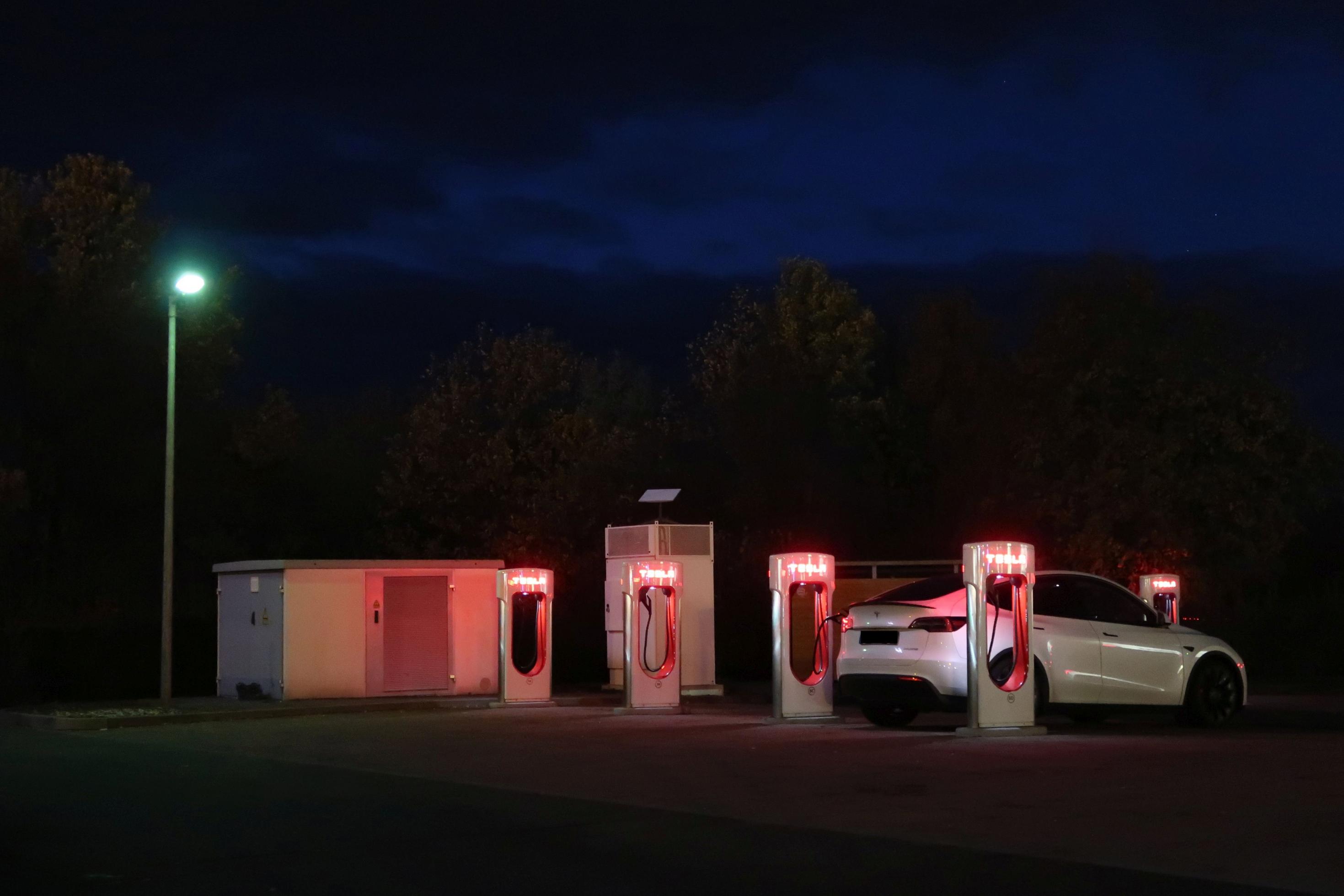 Elektroauto lädt Strom im Dunkeln an einem Tesla-Supercharger.
