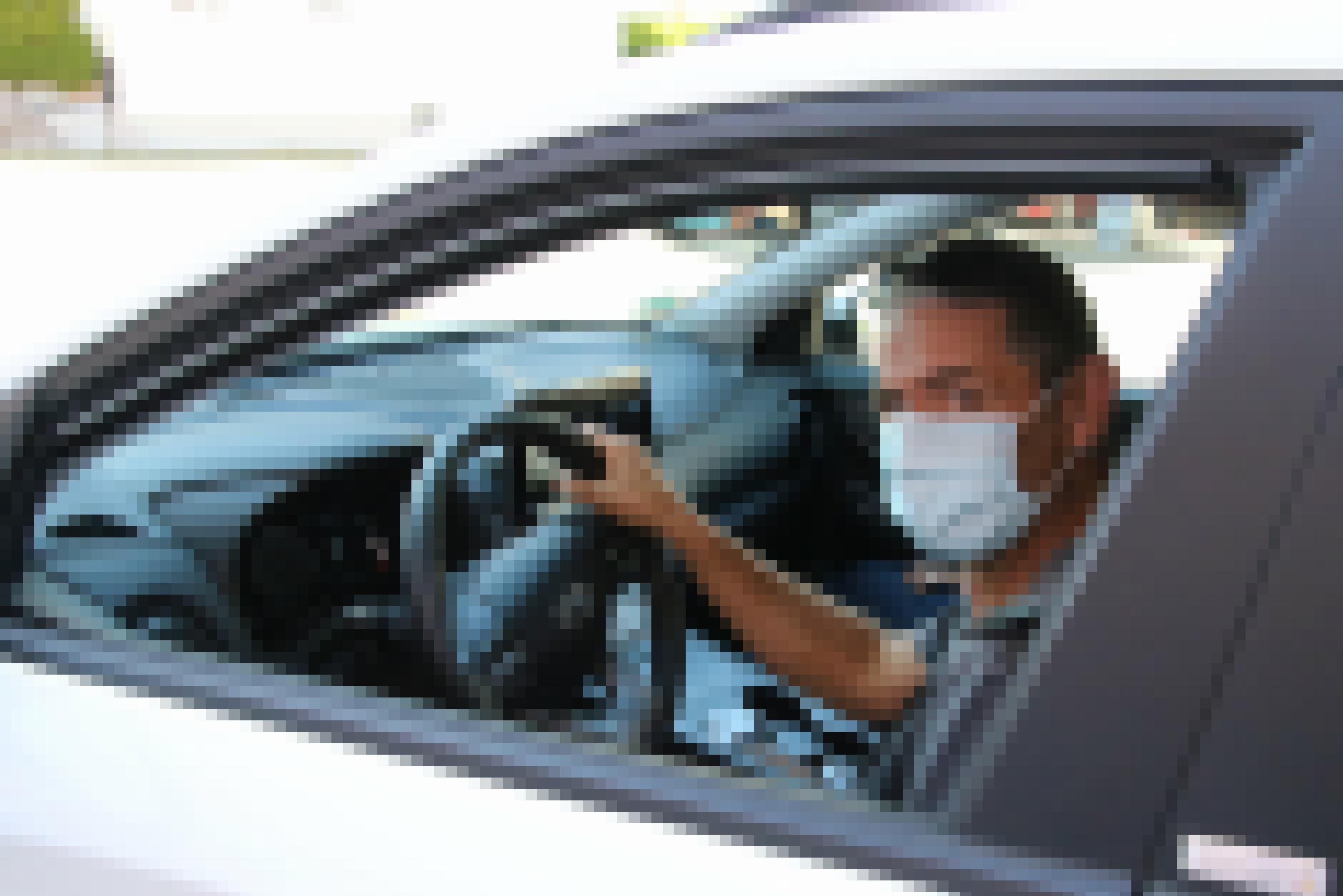 Ein Mann mit Mund-Nase-Schutz sitzt am Steuer eines Fahrzeugs.