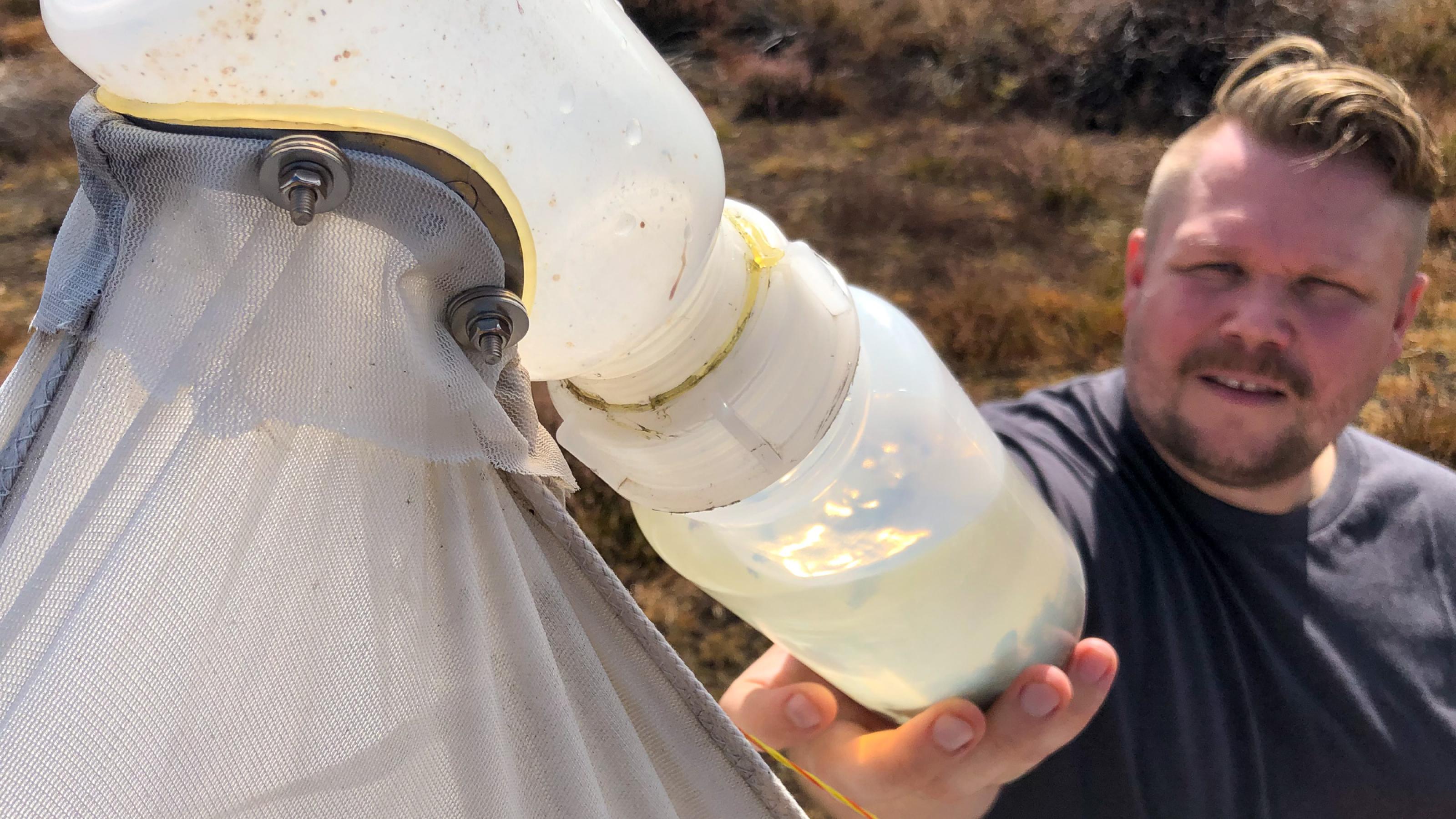Ein Mann hält eine Plastikflasche in der Hand, in der in Alkohol tote tausende Insekten schwimmen.