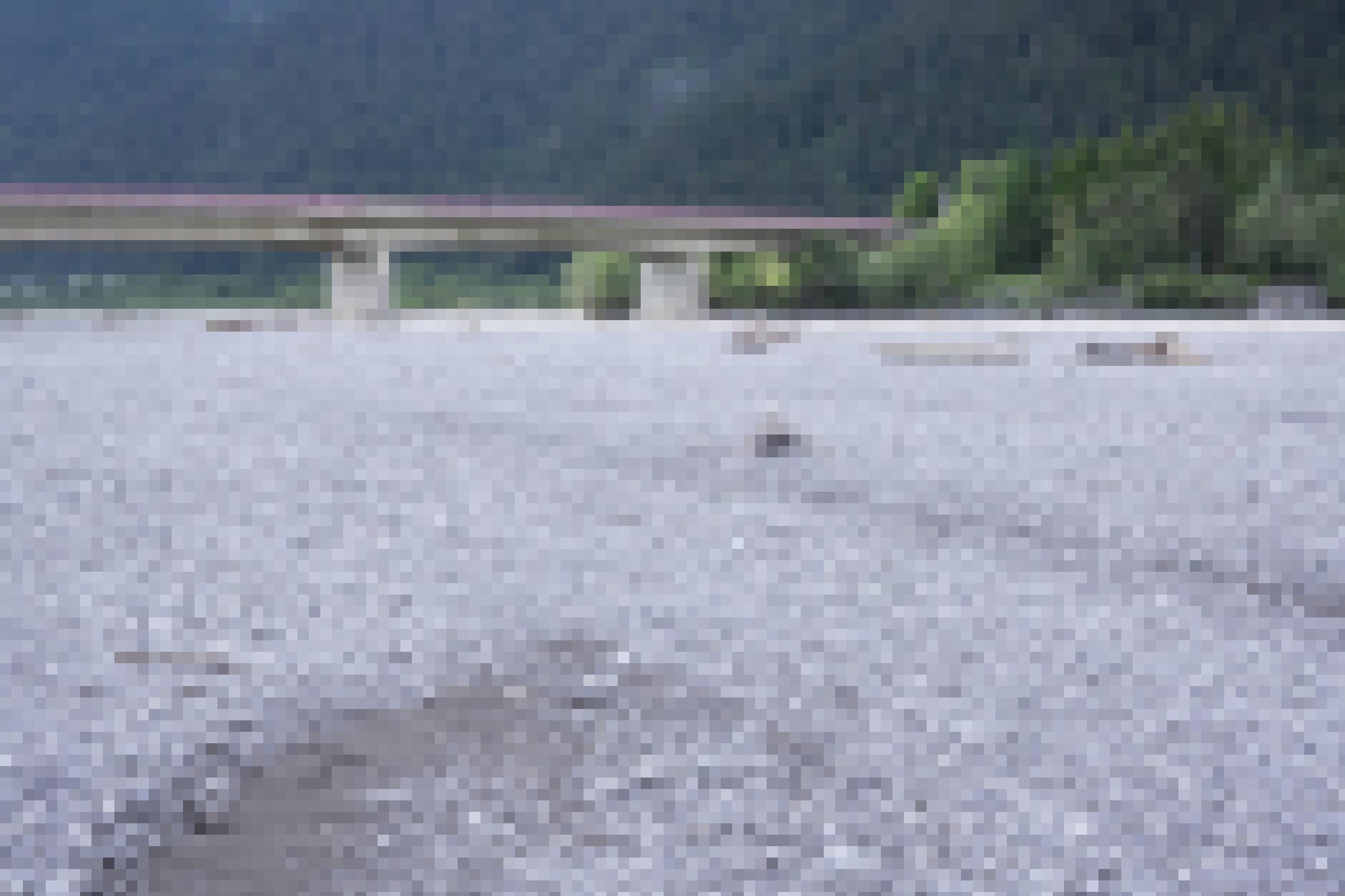 Große Schotterfläche mit Totholz, dahinter die Brücke.