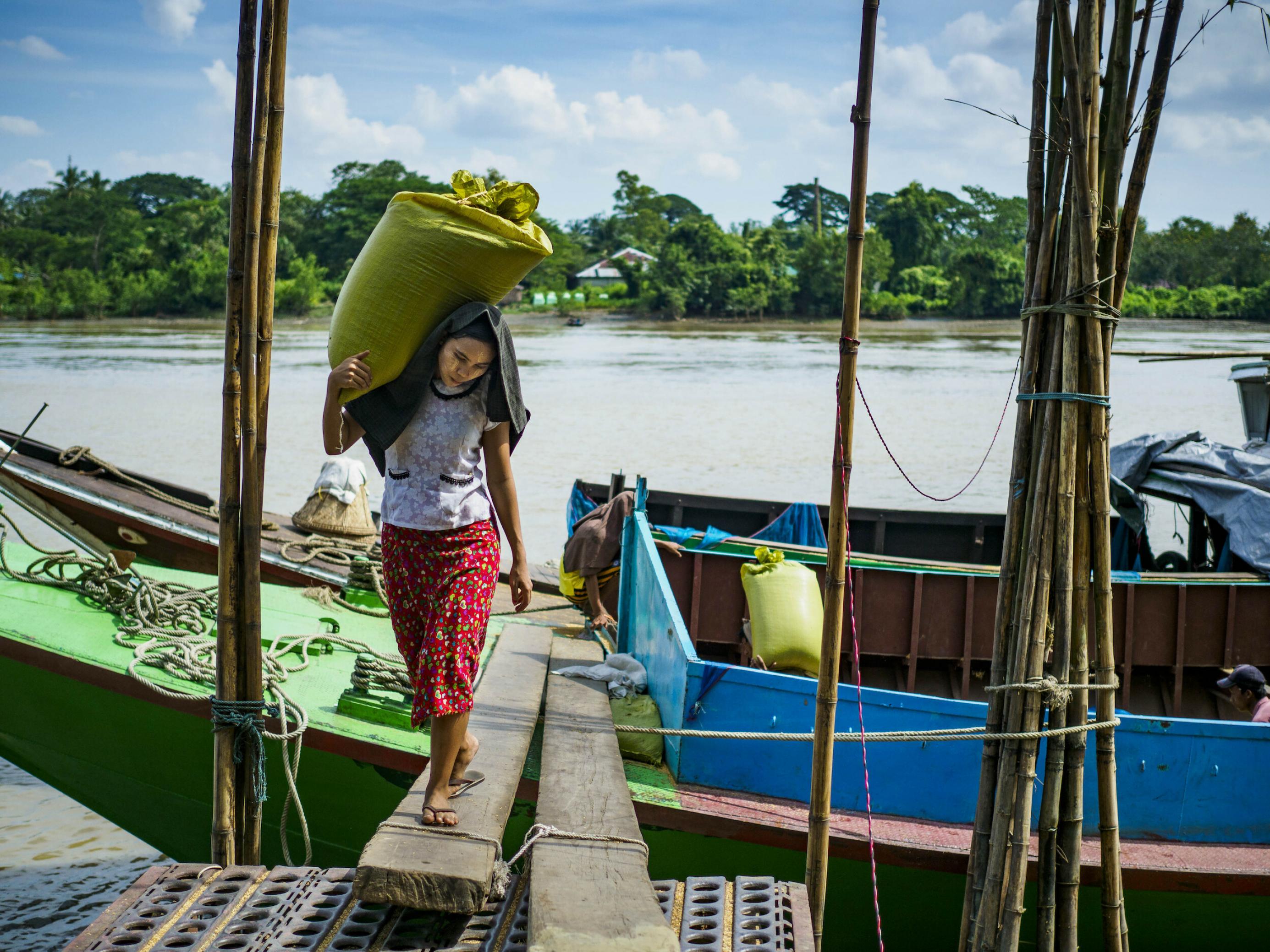 Eine Frau trägt einen Sack Reis von einem Boot am Irawadi-Fluss.