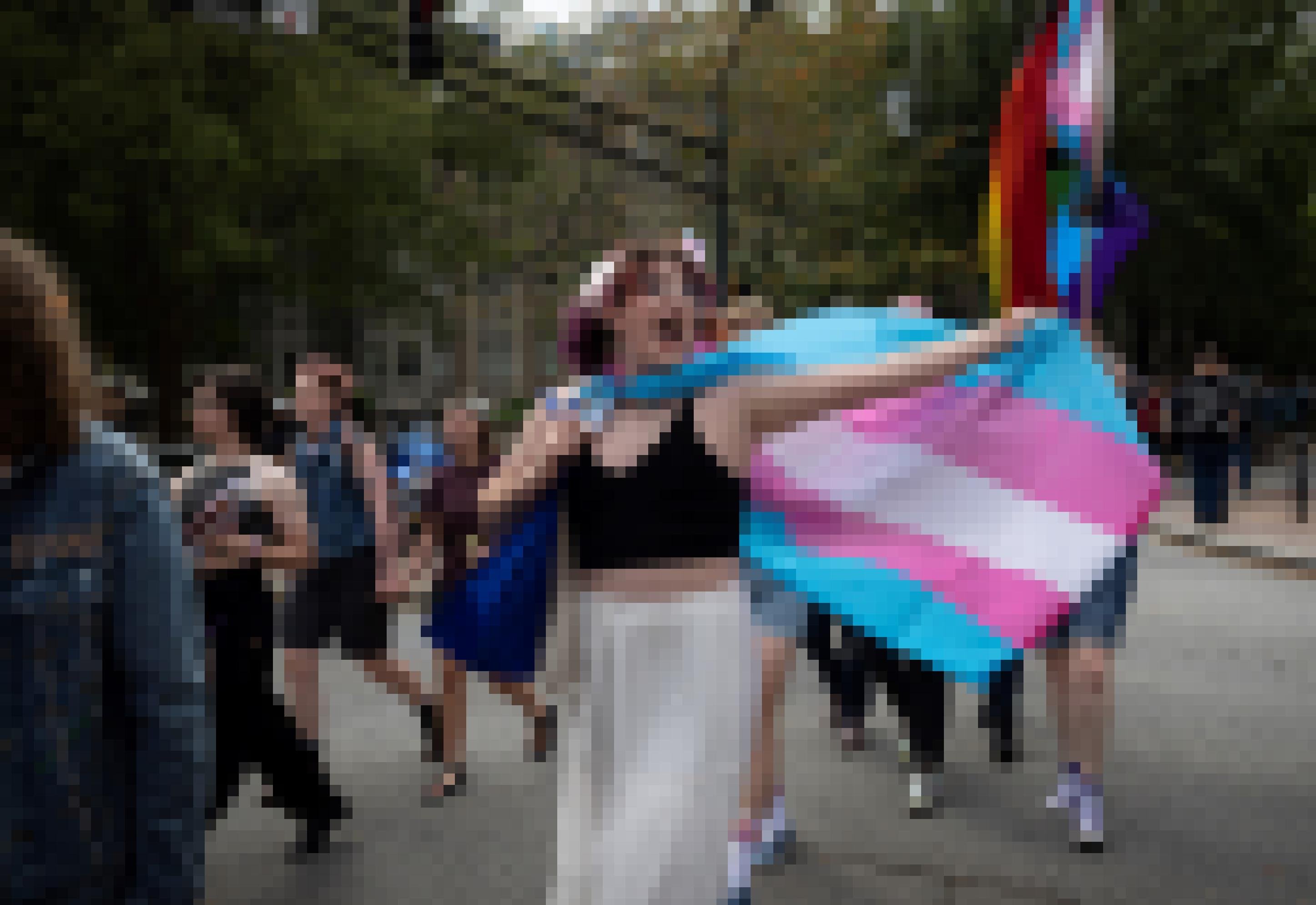 Eine glückliche junge trans Frau tanzt auf einer Pride-Parade und trägt als Umhang eine Transgender-Fahne.