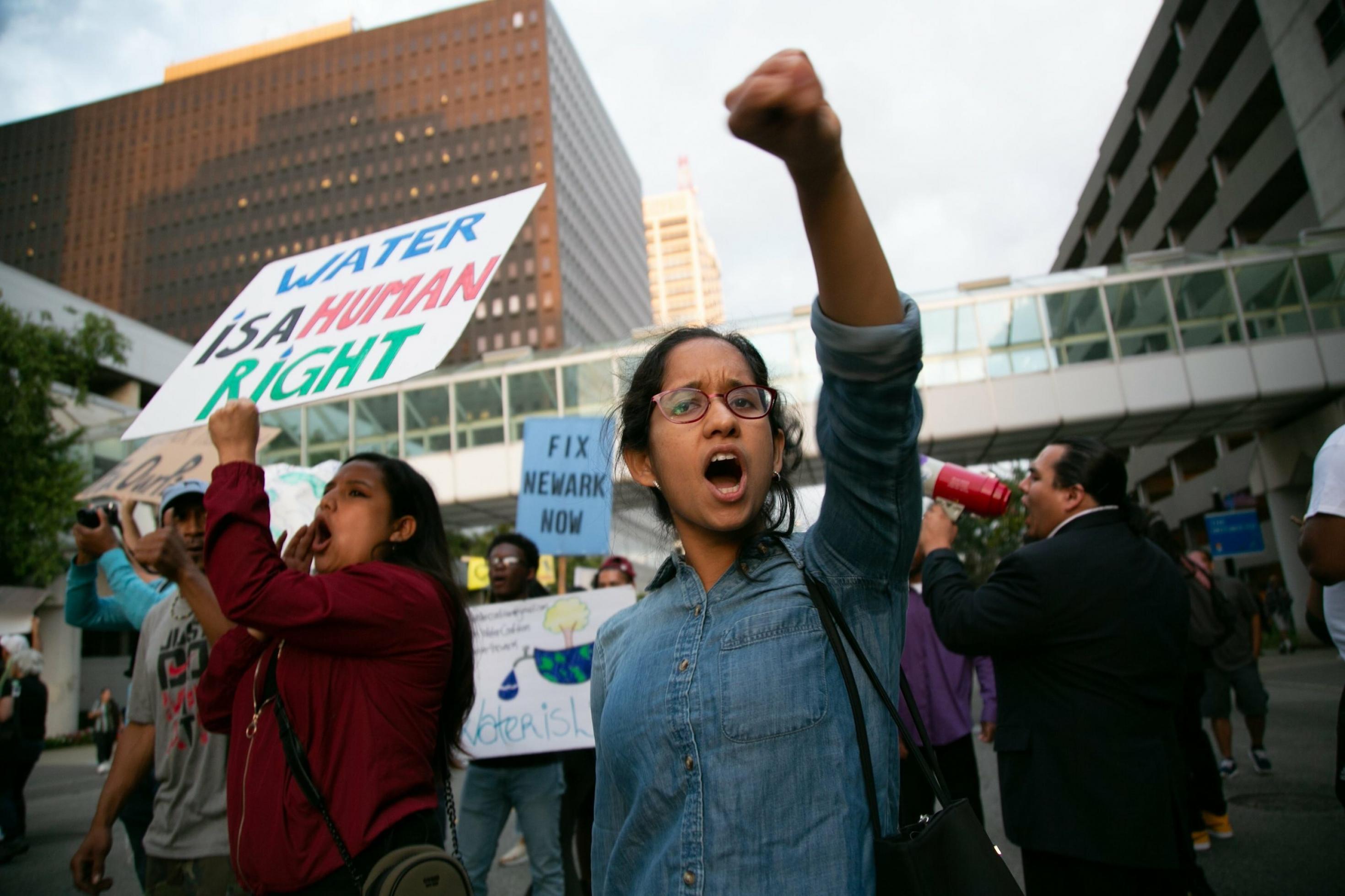 Eine junge Demonstrantin reckt die Faust in die Höhe, während neben ihr eine Frau ein Schild mit der Aufschrift „Water is a human right“ in die Höhe hält.